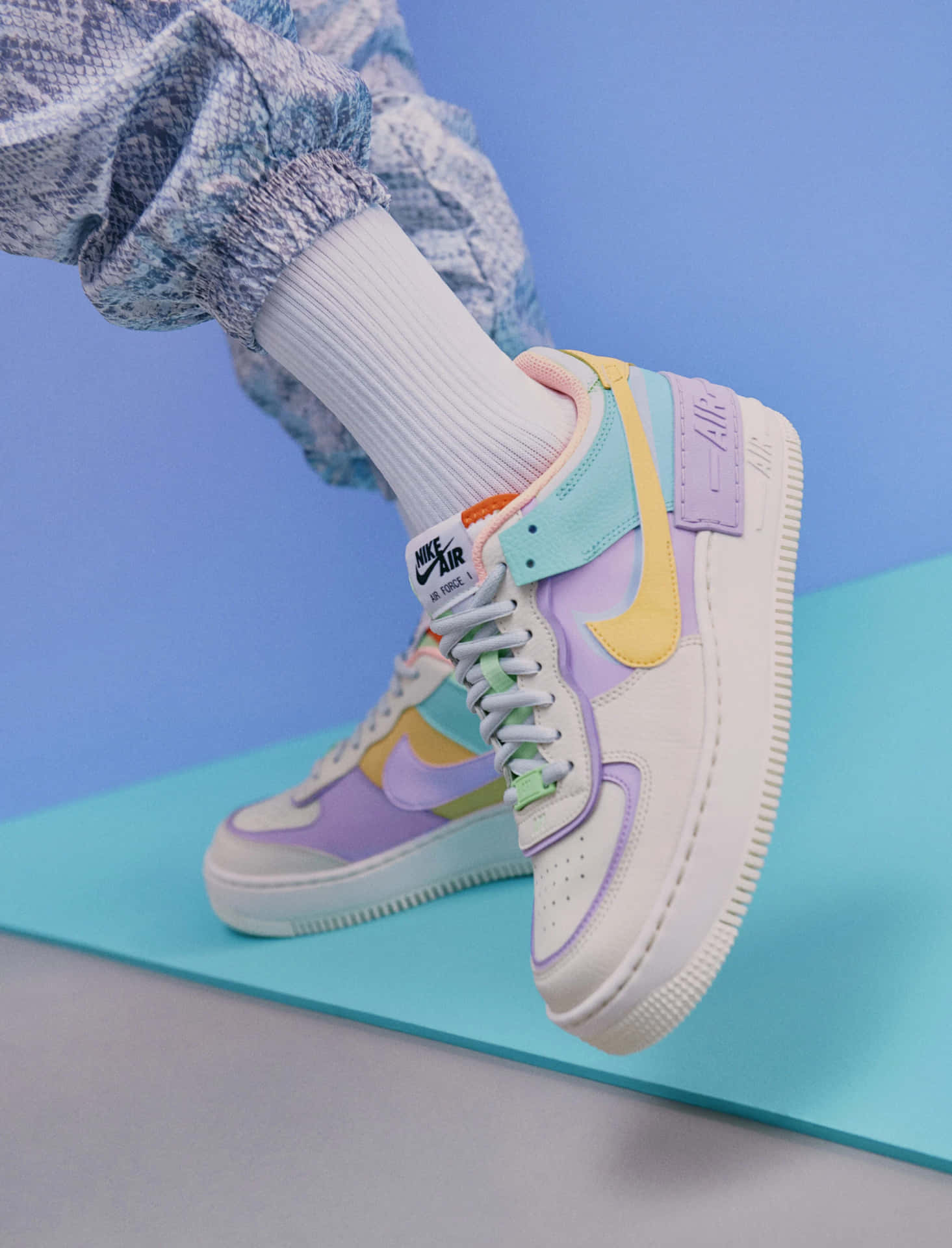 藍色表面上，柔和色調的Nike Air Force 1運動鞋配白色襪子和圖案褲子。