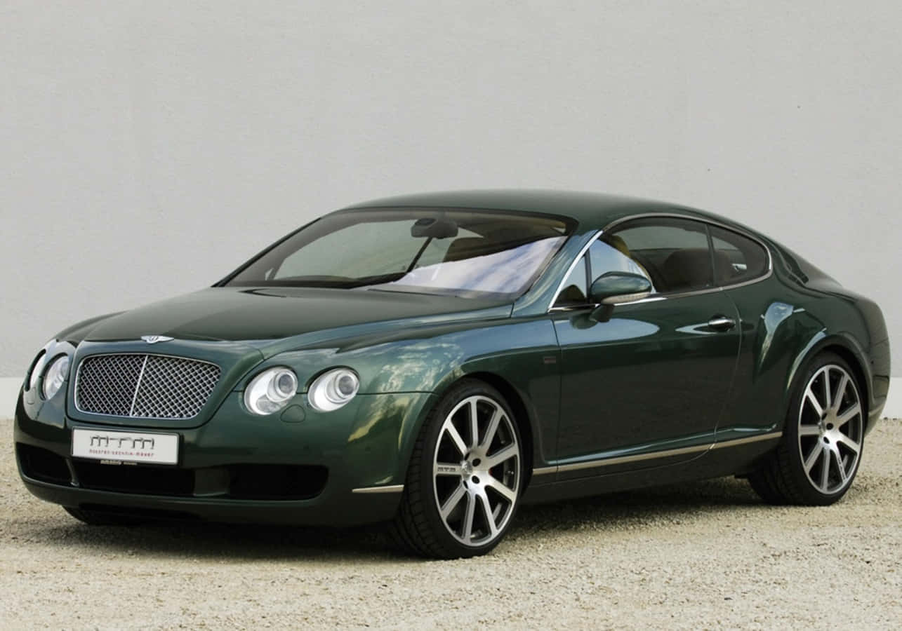 深綠色賓利 Continental GT 雙門轎跑車停在碎石上，背景素色。