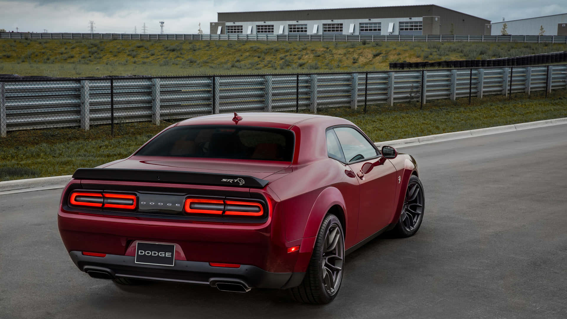 紅色Dodge Challenger SRT Hellcat喺賽車場上，背景有工業建築物。