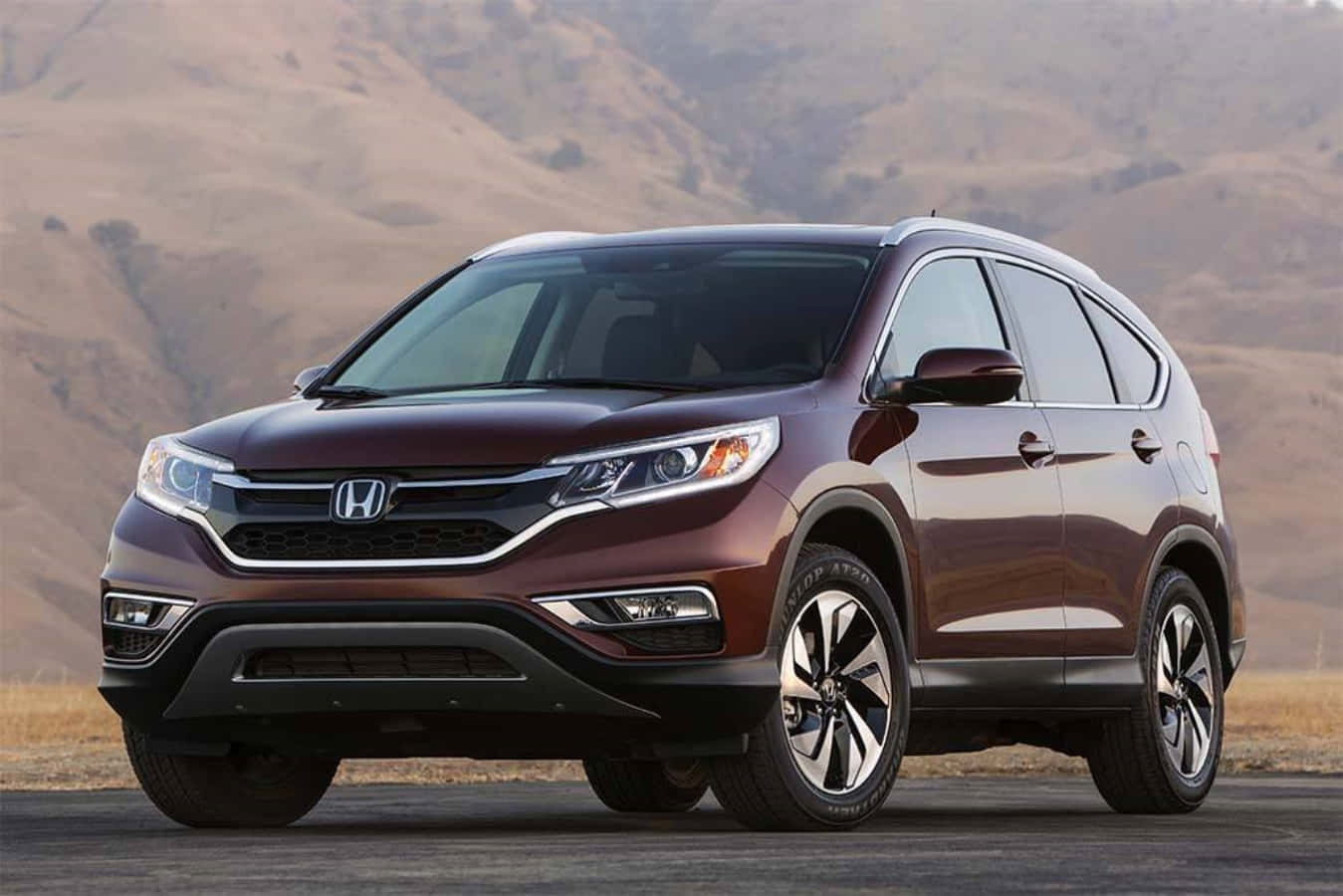 感受Honda的動力 壁紙 — 一架栗色本田CR-V SUV停泊在瀝青路上，背景是乾燥的山丘，在明亮的日光下。