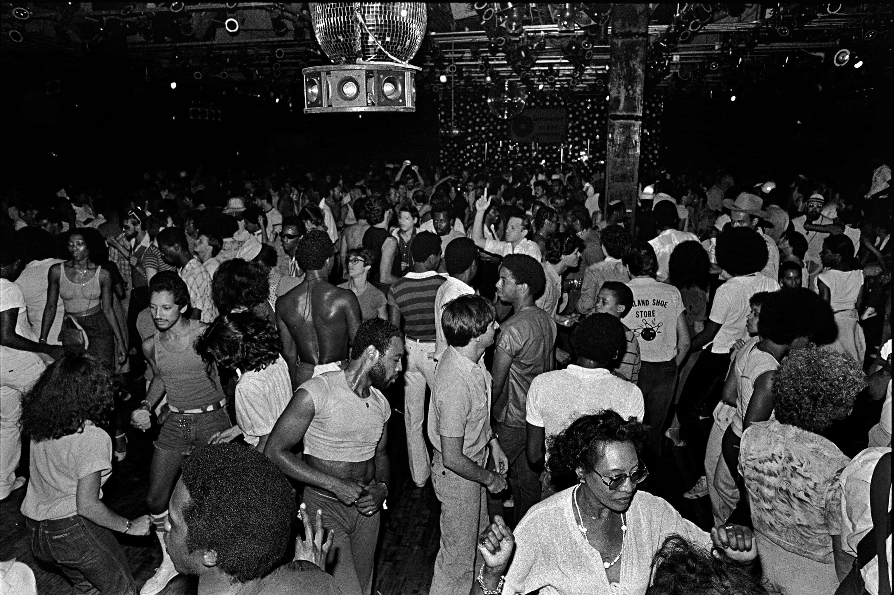 感受八十年代的活力街景 壁紙 — 人群在昏暗的1970年代夜總會中，在迪斯科球下舉手跳舞，充滿活力。