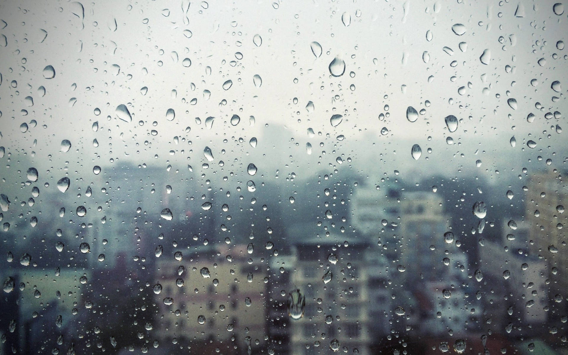 灰色日子裡，窗戶上的雨滴俯瞰著模糊的城市景觀。