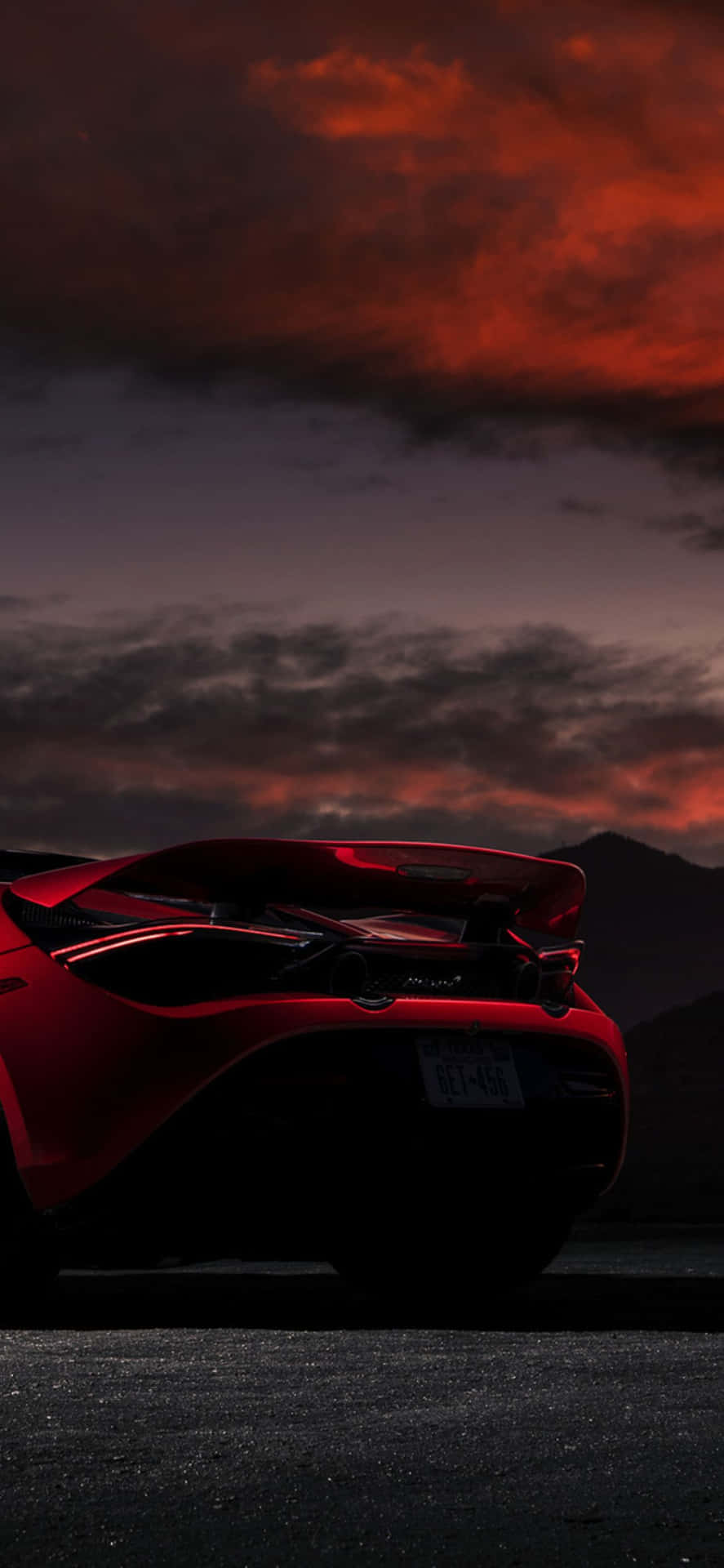 感受奢華與速度的完美結合：iPhone Xs Max與McLaren 720S組合 壁紙 — 一架流線型紅色跑車的剪影，矗立在帶有烏雲的熾熱橙紫色日落天空前。