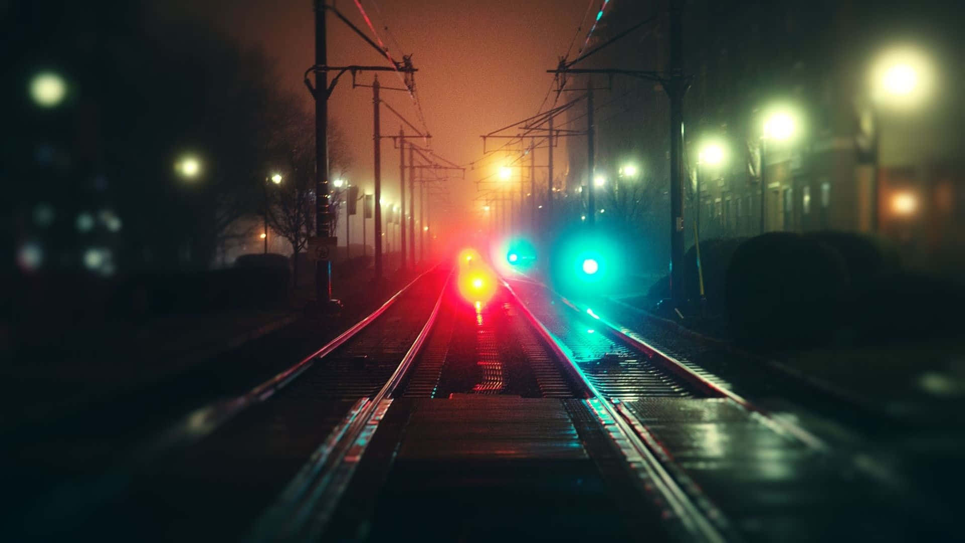 感受寒意 壁紙 — 霧夜鐵軌在溫暖街燈下匯聚向發光的紅綠火車信號燈。