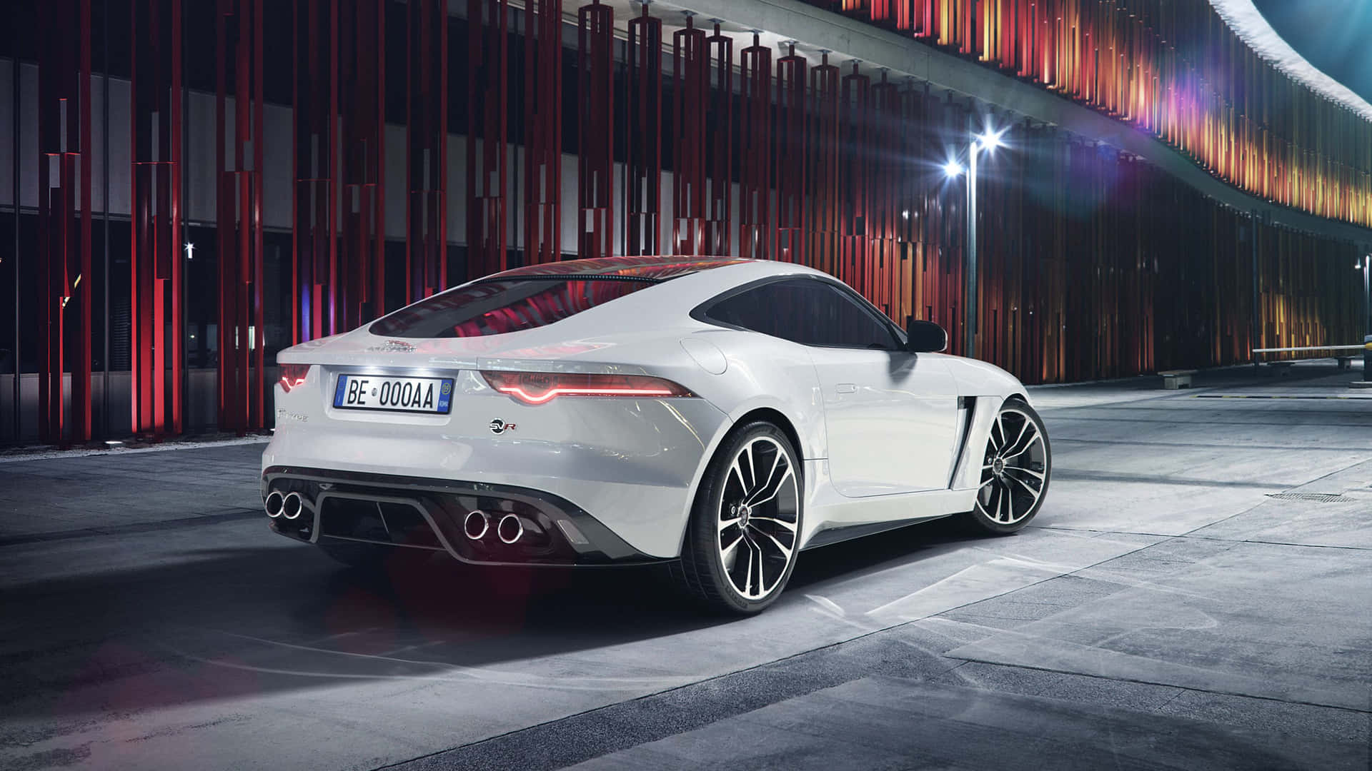 白色Jaguar F-Type跑車夜間停放在霓虹燈下，靠近現代建築。
