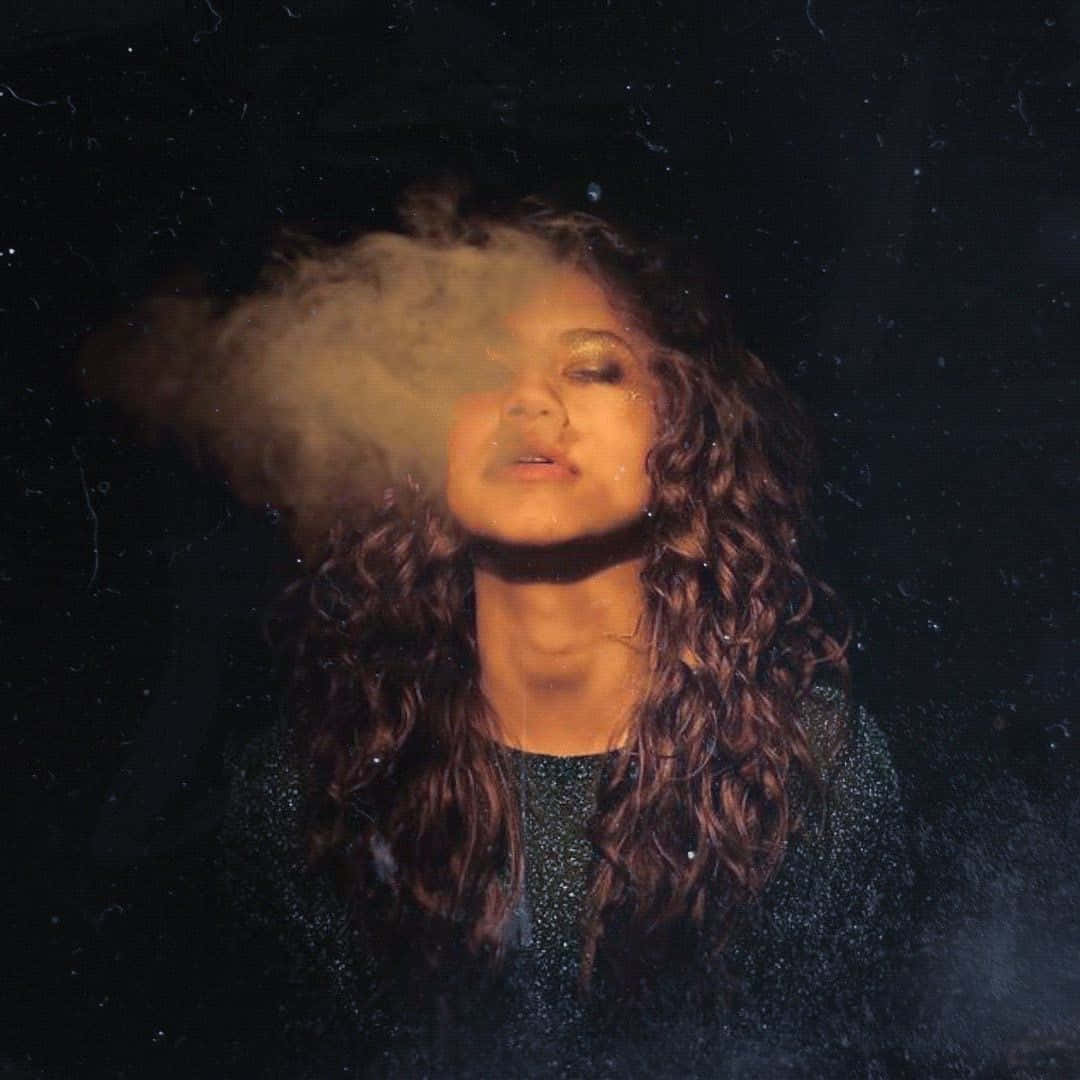 感受愉悅的自由 壁紙 — 一位捲髮女性在昏暗星空背景下，柔和燈光中呼出一縷煙霧。