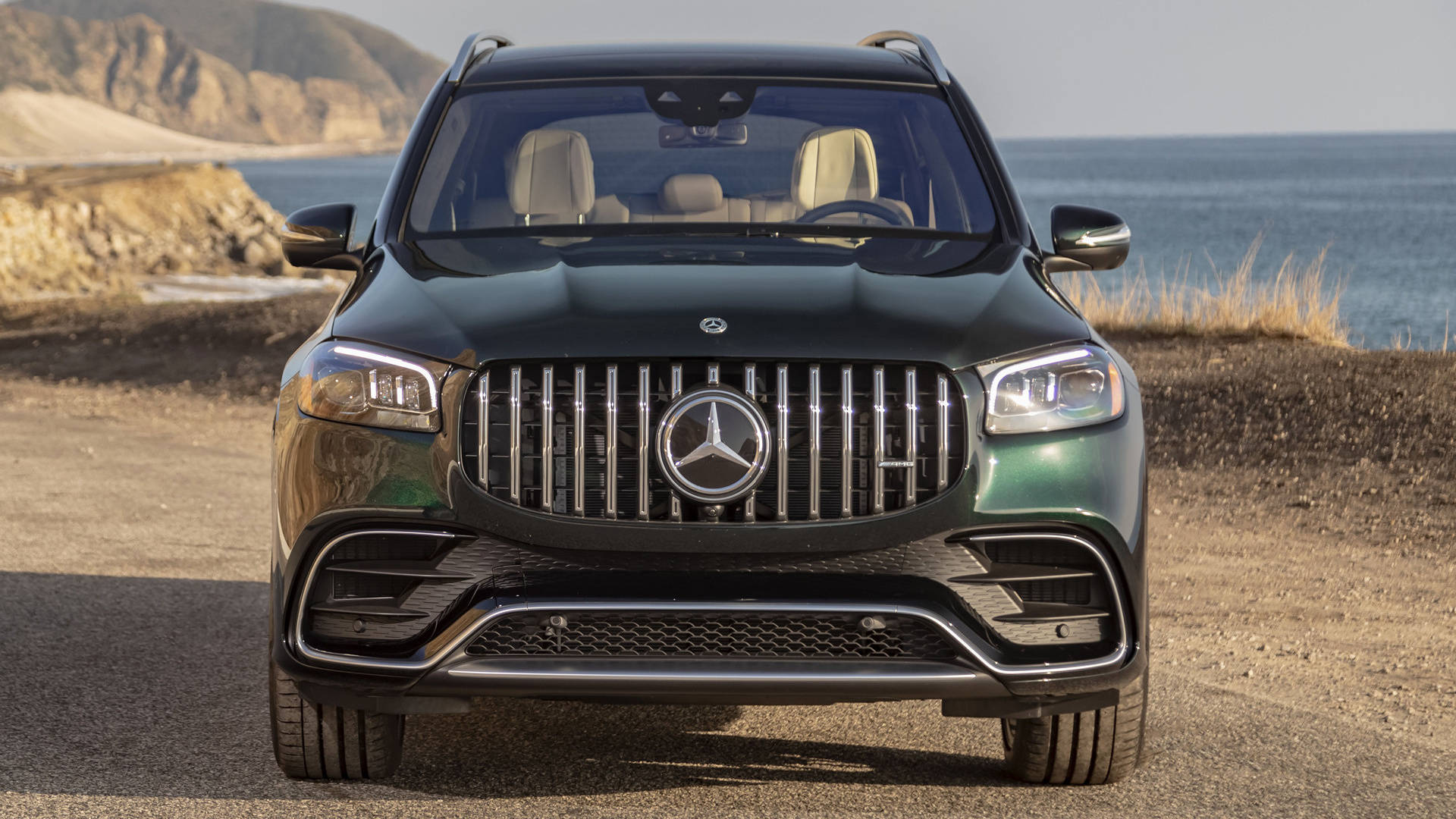 一架綠色平治 GLS SUV 停泊喺沿海泥路嘅正面視圖。