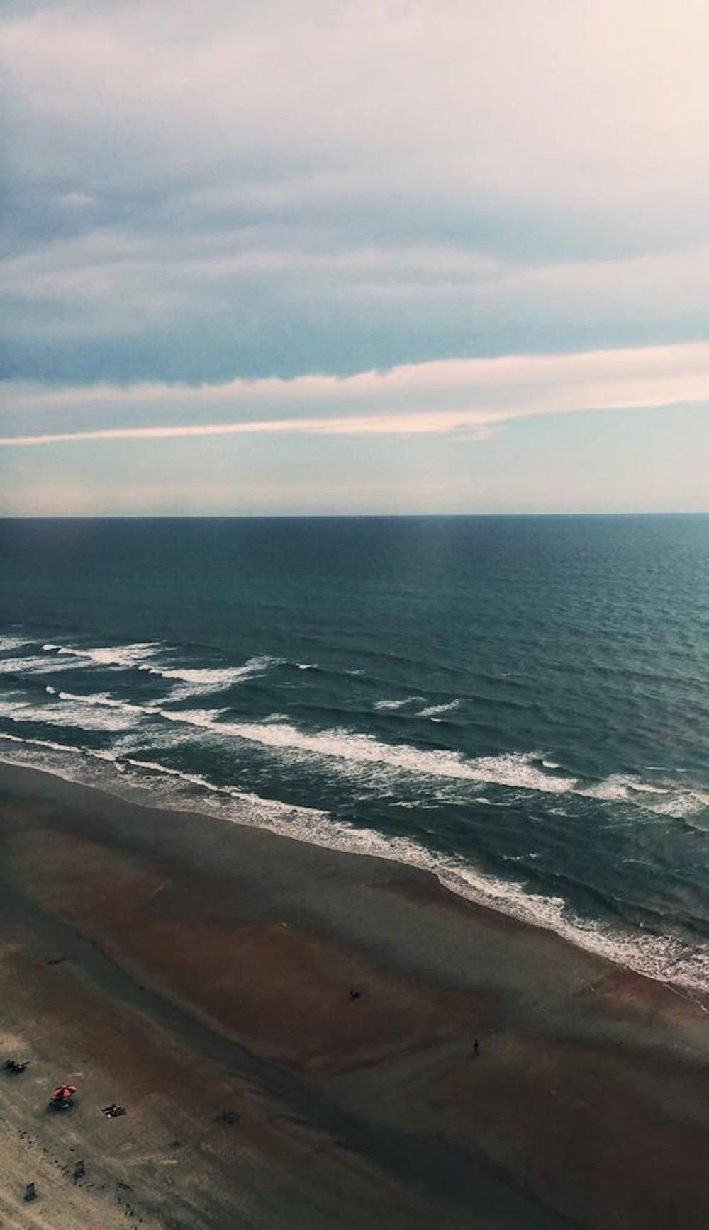 鳥瞰海洋波浪在沙灘上拍打，天空多雲。