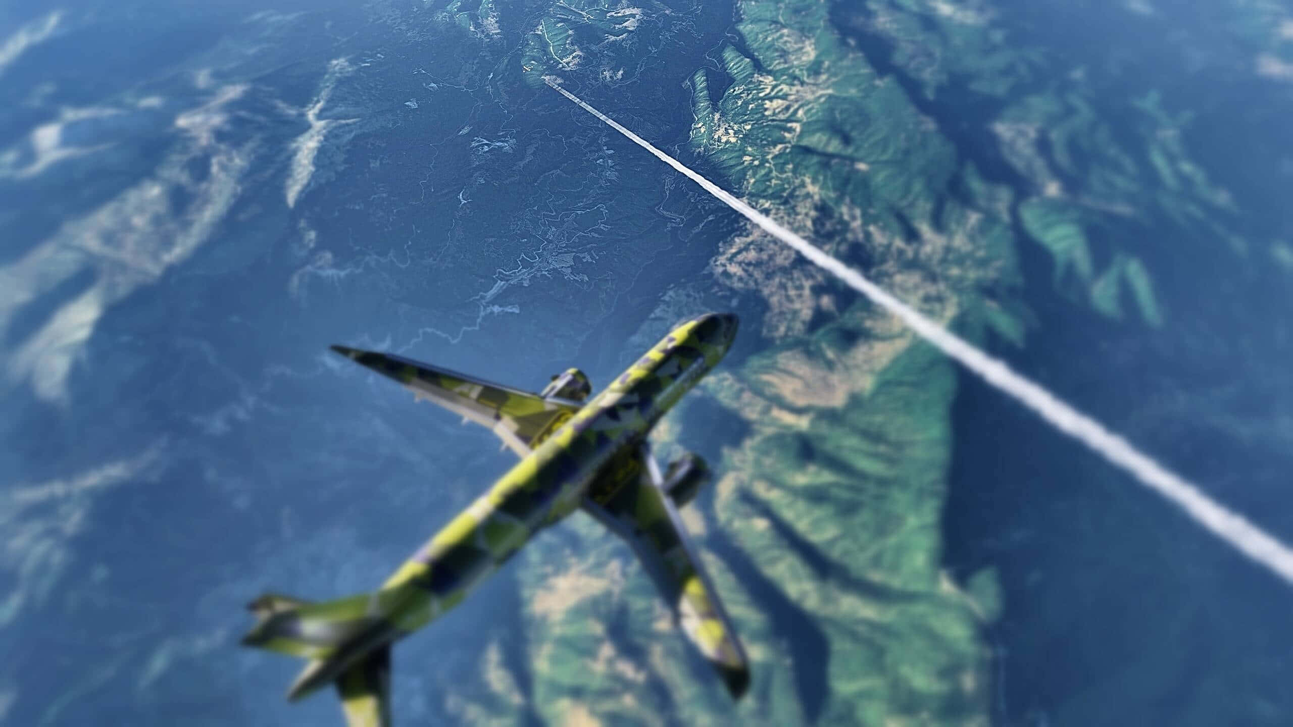 感受自由之風 壁紙 — 一架迷彩飛機翱翔於山區地形上空，在藍天中留下一道白色凝結尾跡。