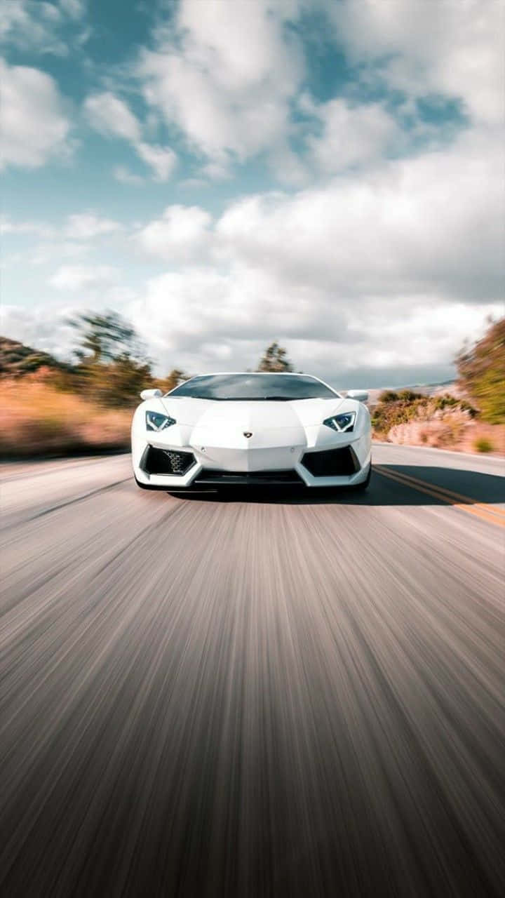 感受賽車的強大動力 壁紙 — 一輛白色林寶堅尼Aventador在部分多雲的天空下，沿著蜿蜒的道路高速行駛，帶有模糊的動態效果。