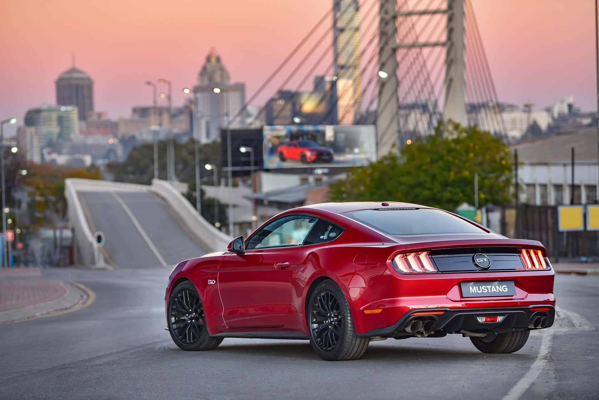 日落時分在城市橋樑上行駛的紅色Mustang GT。