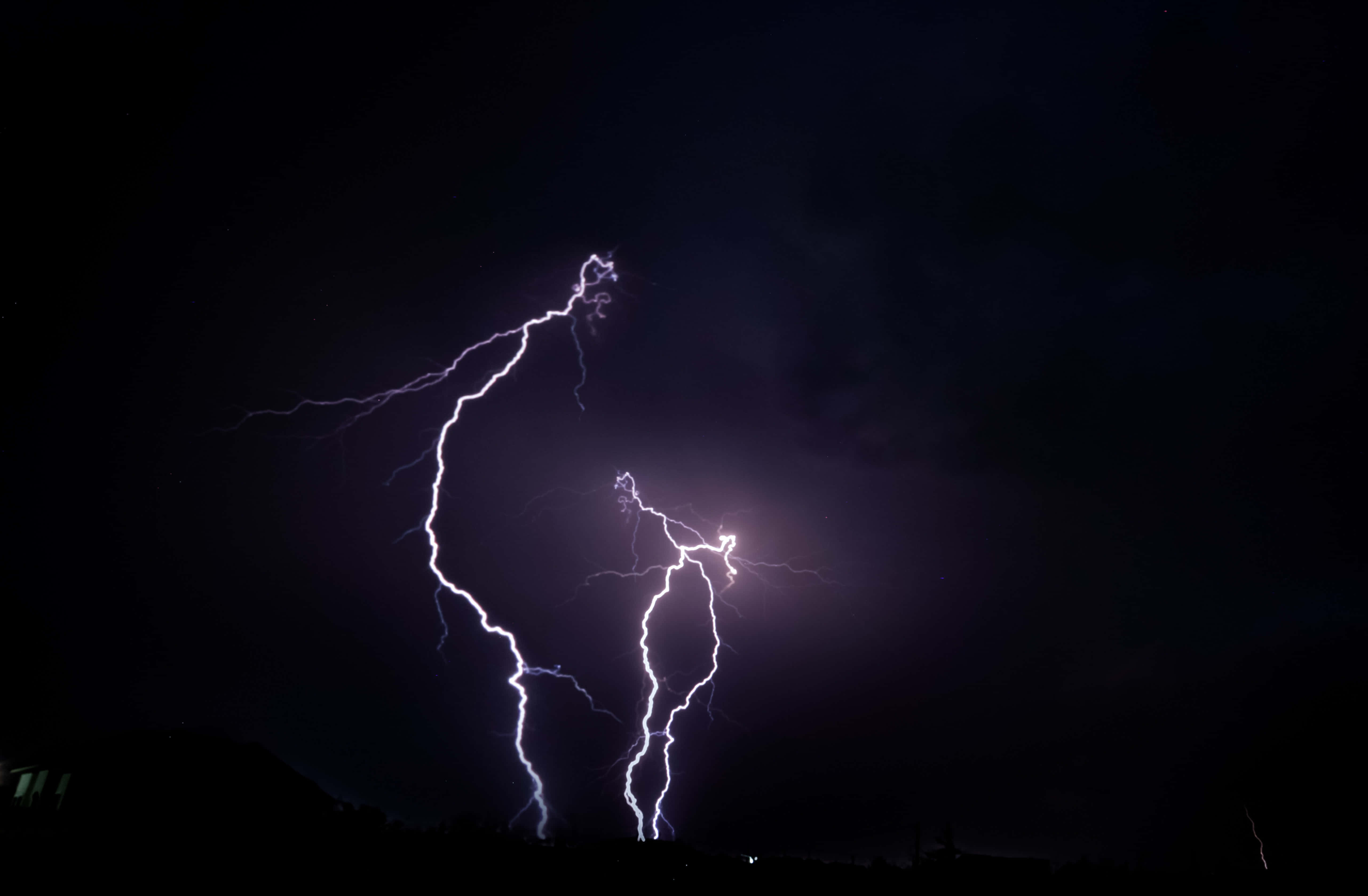 感受閃電的力量 壁紙 — 一道強勁的閃電在黑暗的夜空中分叉，劃過剪影般的地景。