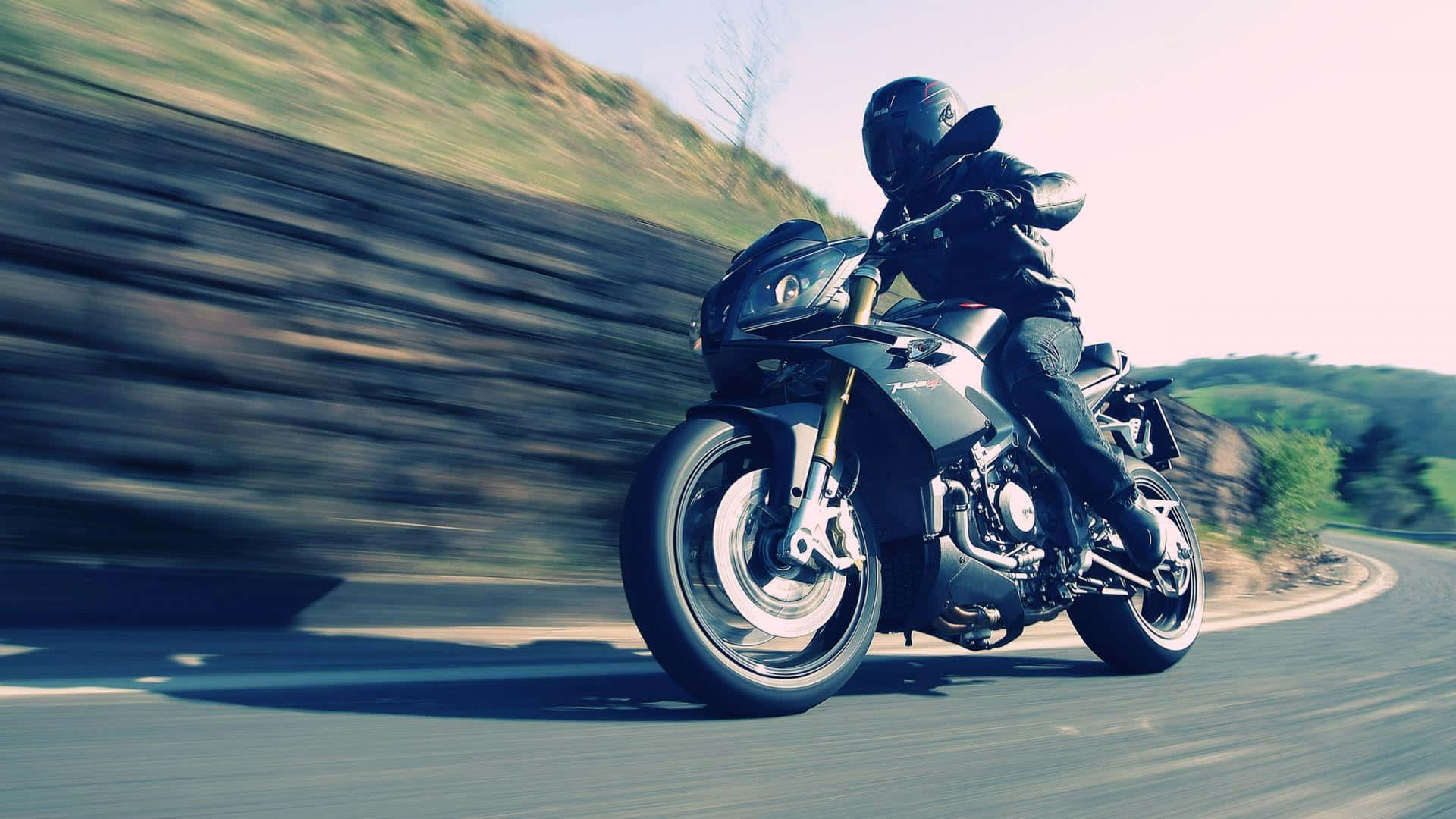 感受開闊道路的自由 壁紙 — 電單車手在蜿蜒道路上傾身入彎，動態模糊傳達高速與冒險感。