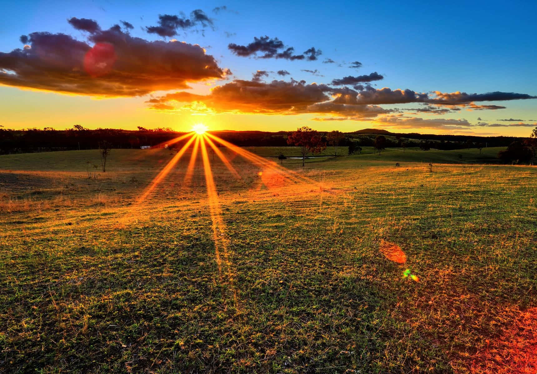 夕陽照耀草地，金色光芒與彩色雲朵。