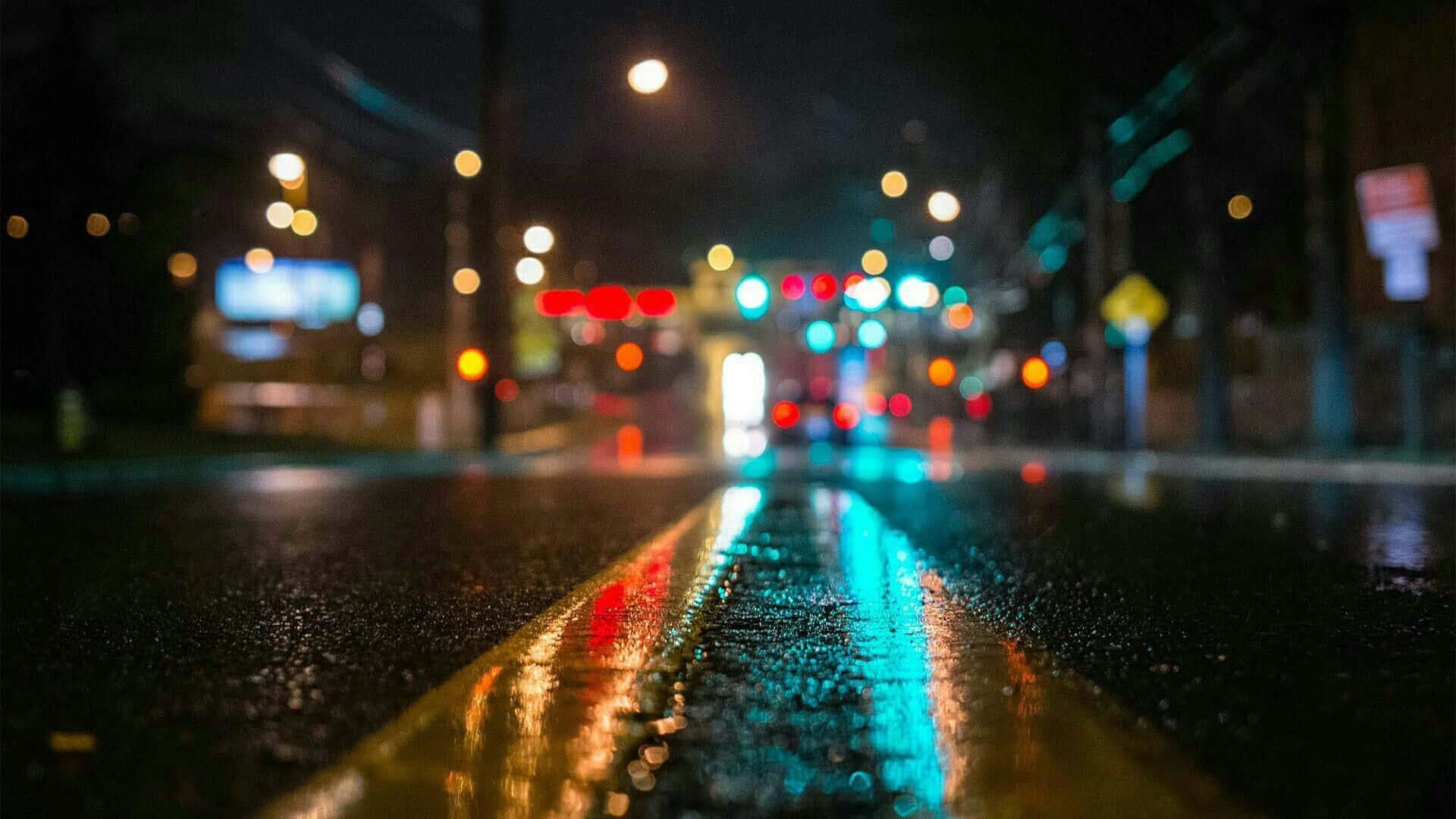雨夜街道，模糊的燈光反射在濕路面和黃色中心線上。