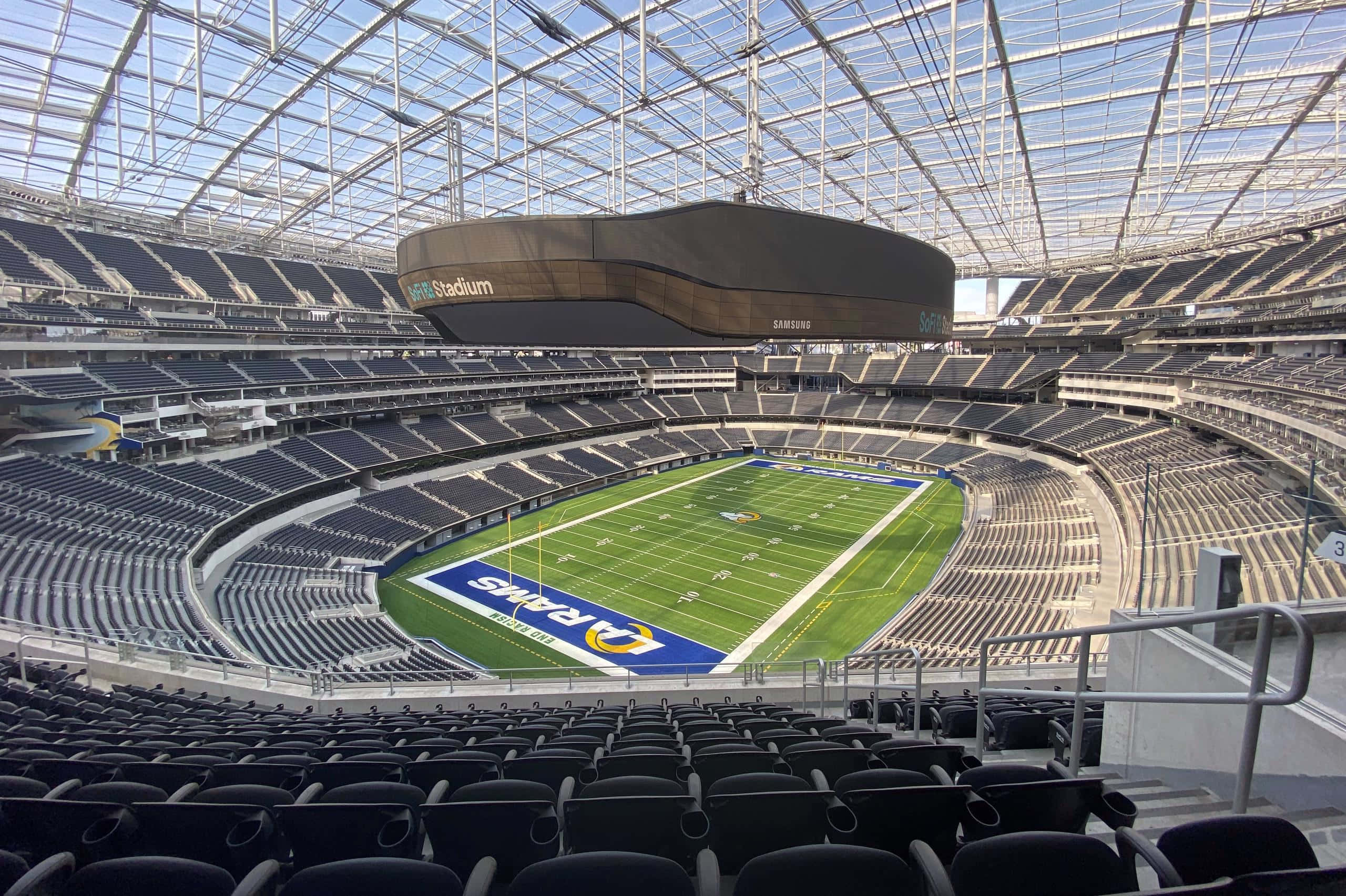 「感受雷鳴：體驗SoFi Stadium」 壁紙 — 空蕩蕩的現代足球場鳥瞰圖，綠色球場和黑色座椅在玻璃屋頂下。