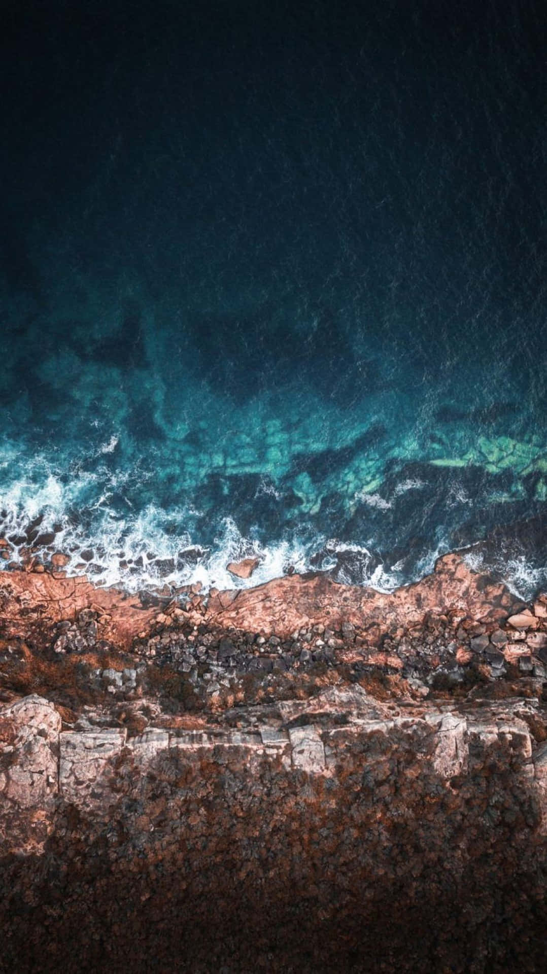 從空中俯瞰，綠松石色的海浪拍打著崎嶇的棕色懸崖。