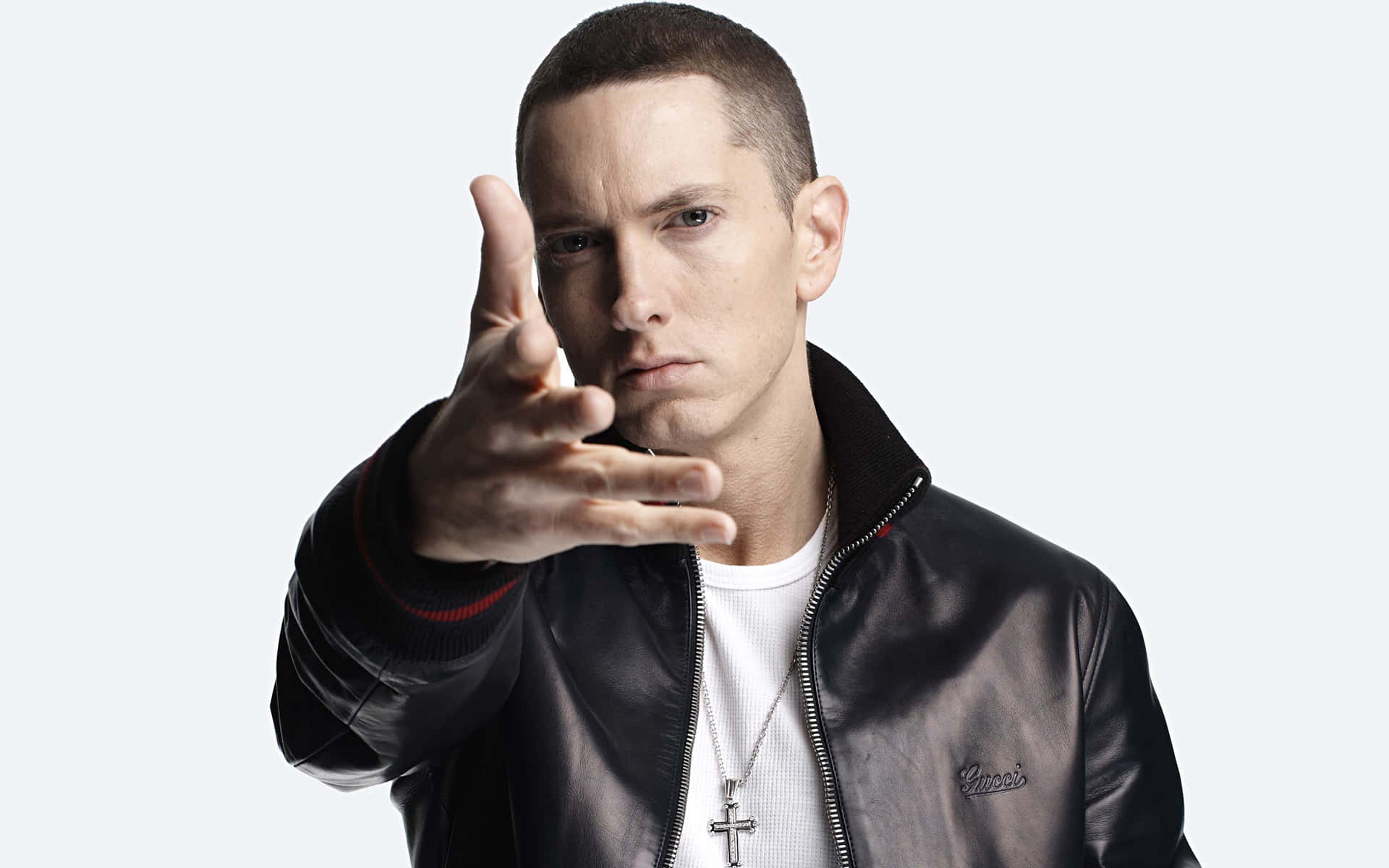 Eminem 身穿黑色皮夾克，戴著十字架項鍊，手指指向相機。