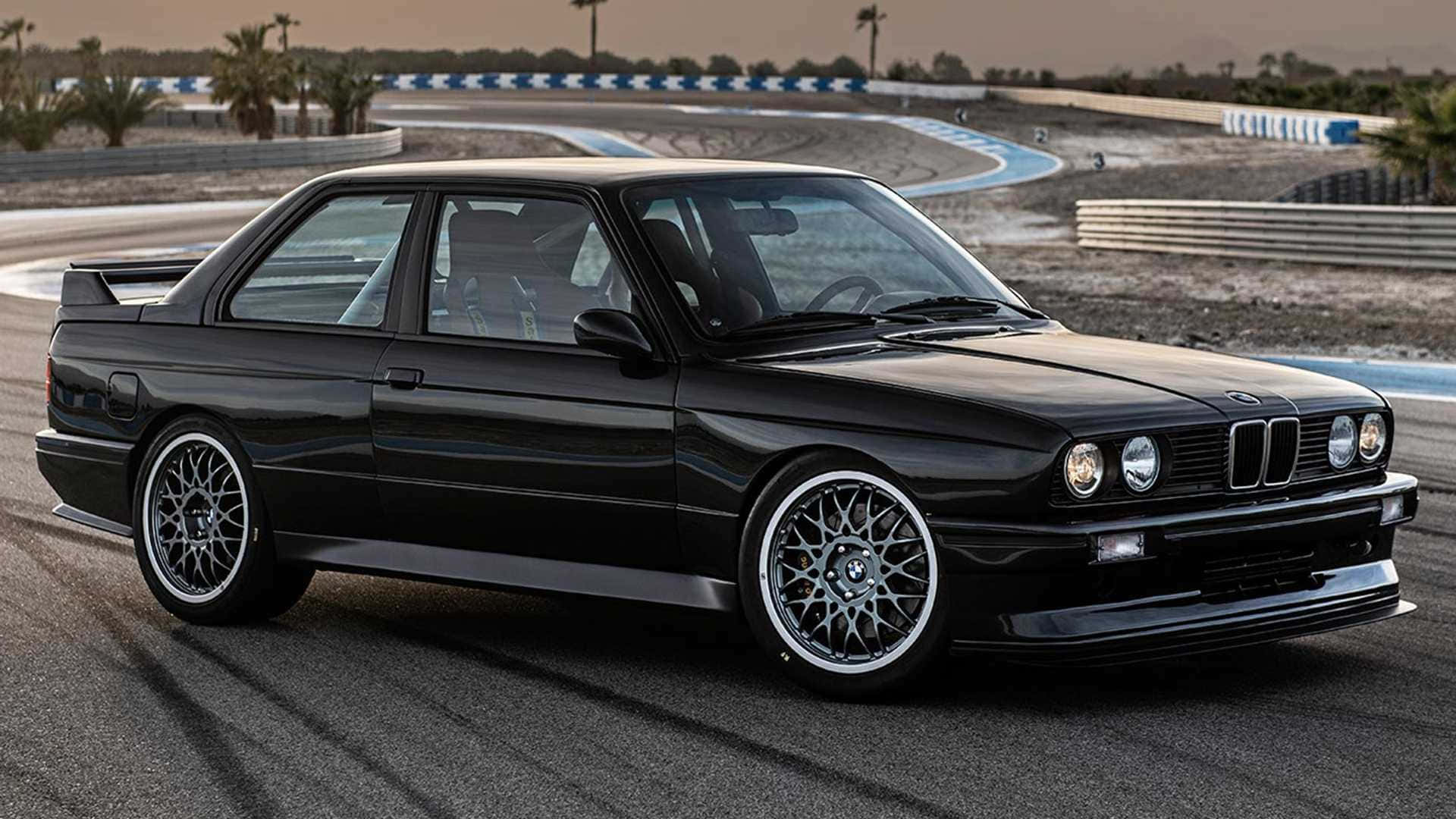 感受駕駛BMW的澎湃力量 壁紙 — 一架時尚的黑色BMW E30雙門轎跑車停在沙漠賽道上，背景有棕櫚樹和藍白色路緣。