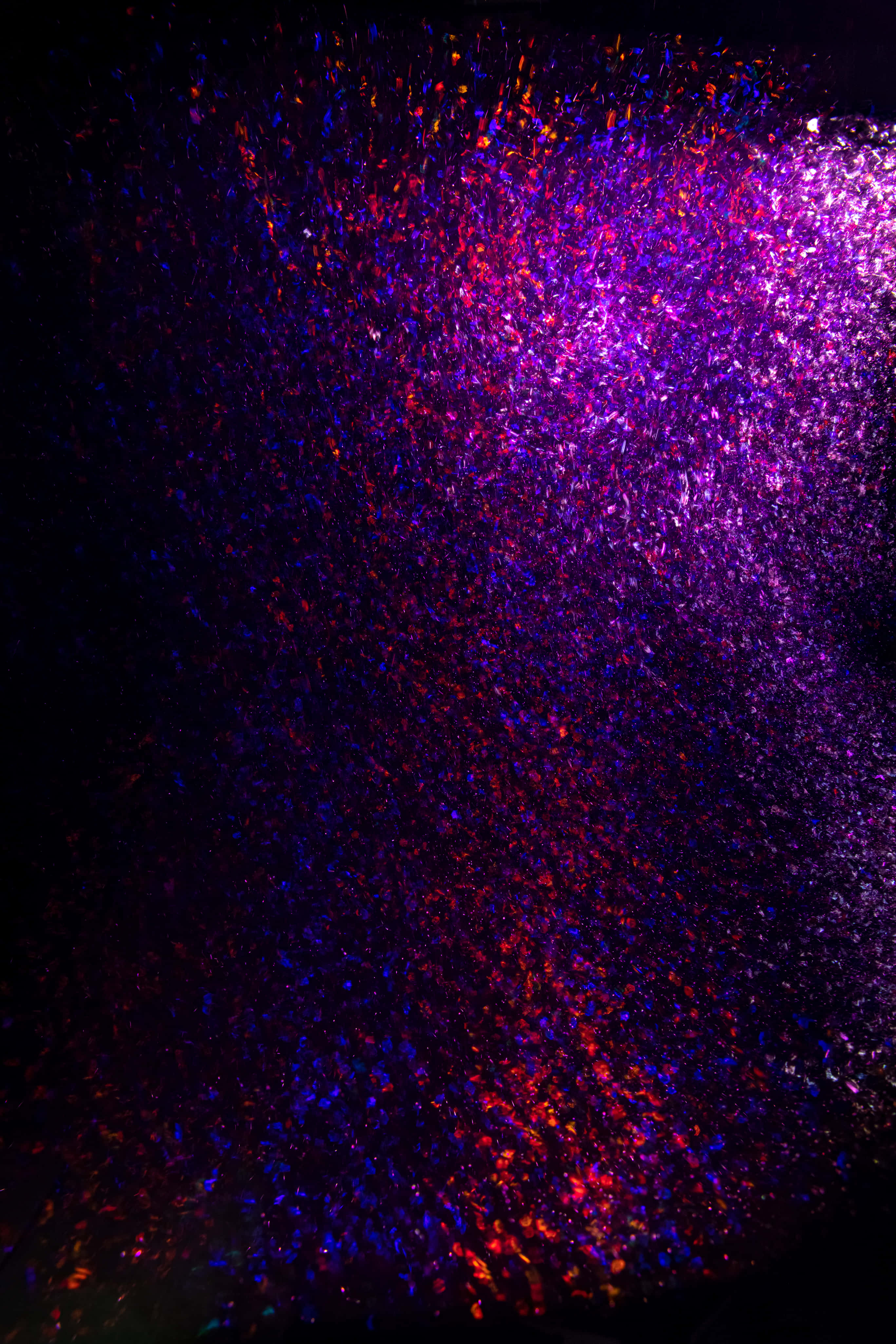 感受魔法般的閃耀背景 壁紙 — 充滿活力的紫色和紅色閃粉粒子在黑色背景上爆炸，形成耀眼的宇宙爆發。