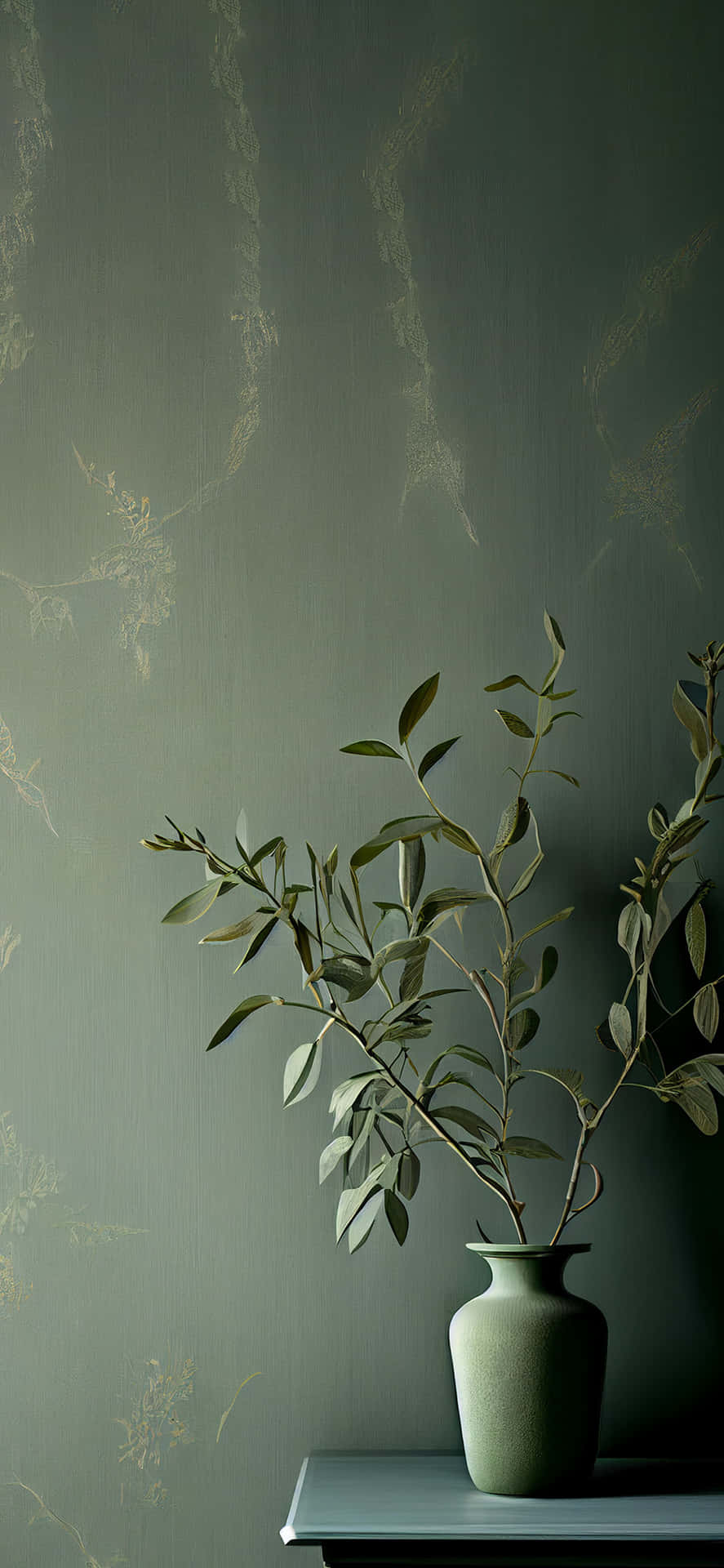 一個綠色花瓶插著橄欖枝放在架子上，背景是有圖案的牆紙。
