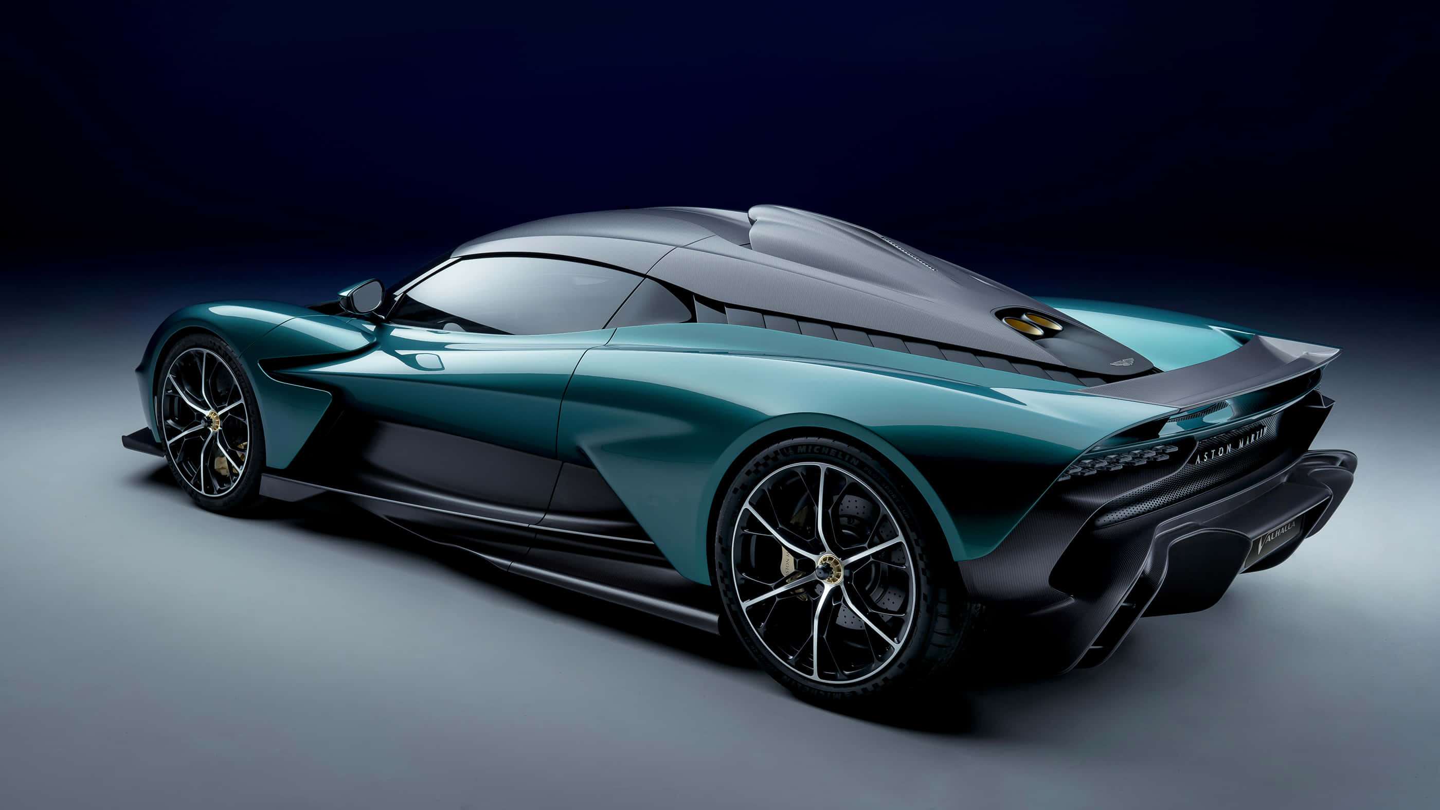 態度即擁有 — Aston Martin 壁紙 — 一部時尚的藍綠色和黑色超跑，具有空氣動力學曲線和發光裝飾，在黑暗的攝影棚背景下展示。