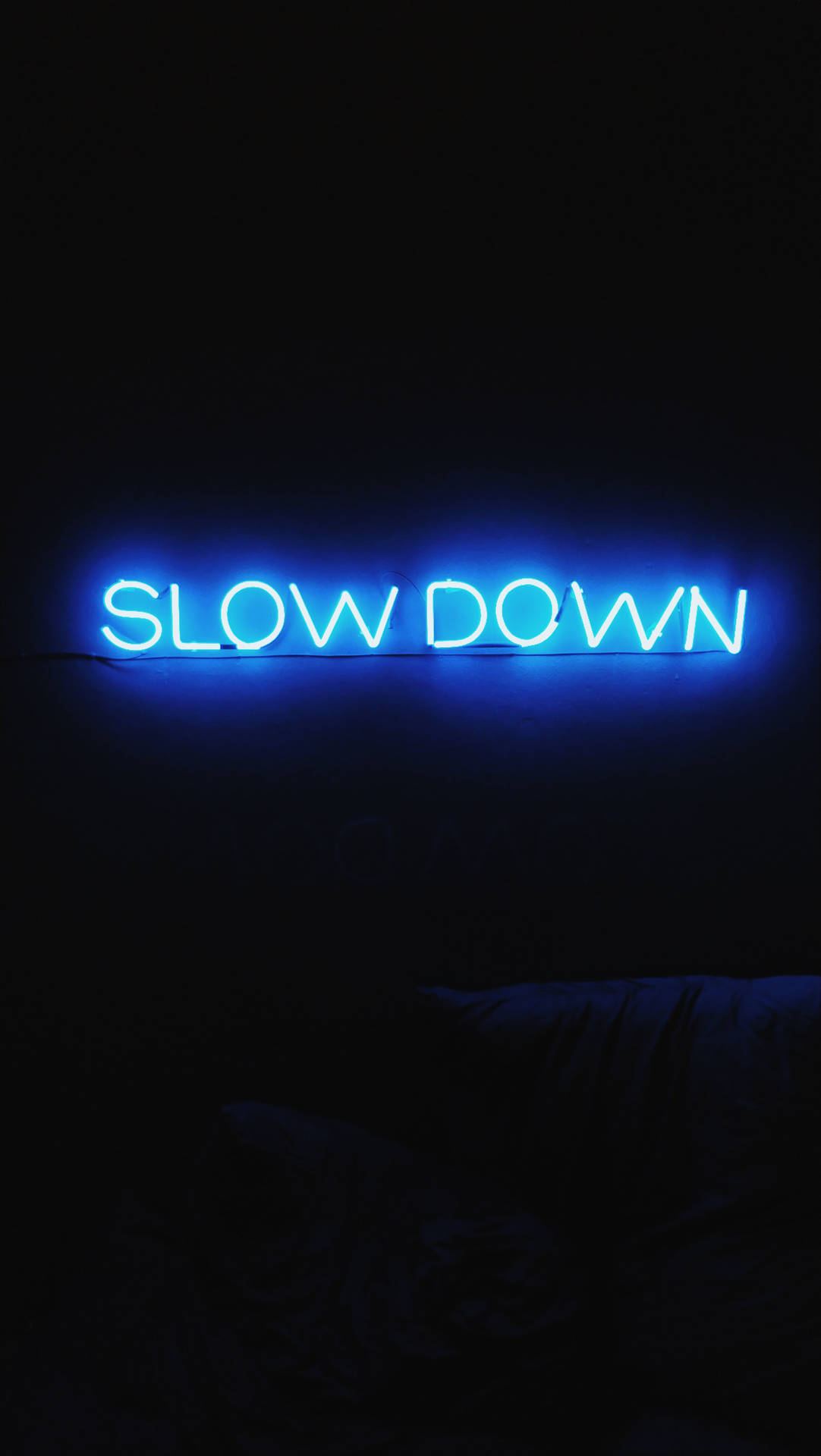在黑暗臥室中寫著 slow down 的藍色霓虹燈牌。
