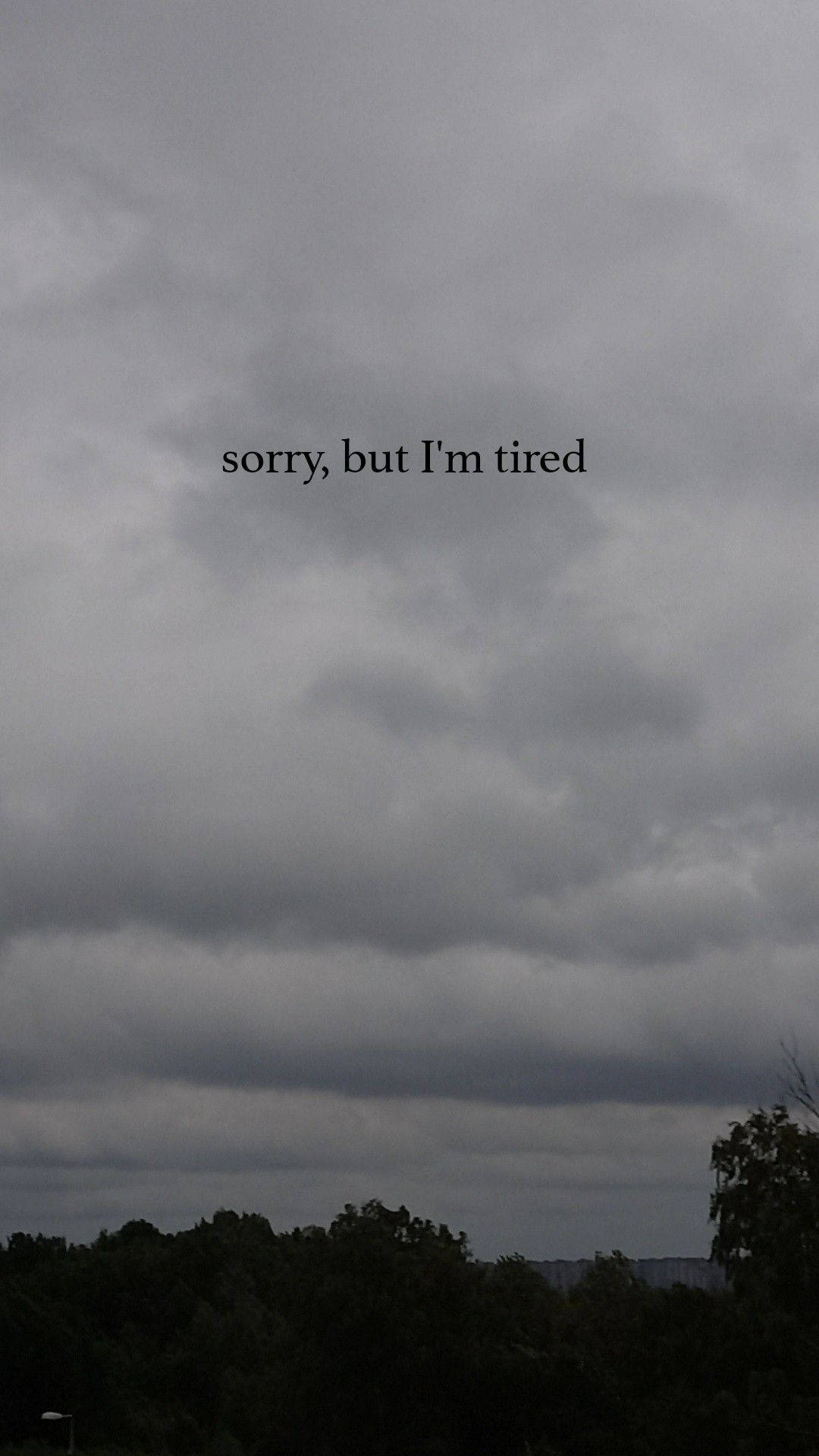 樹木線條上方的陰暗多雲天空，帶有文字「sorry but I'm tired」