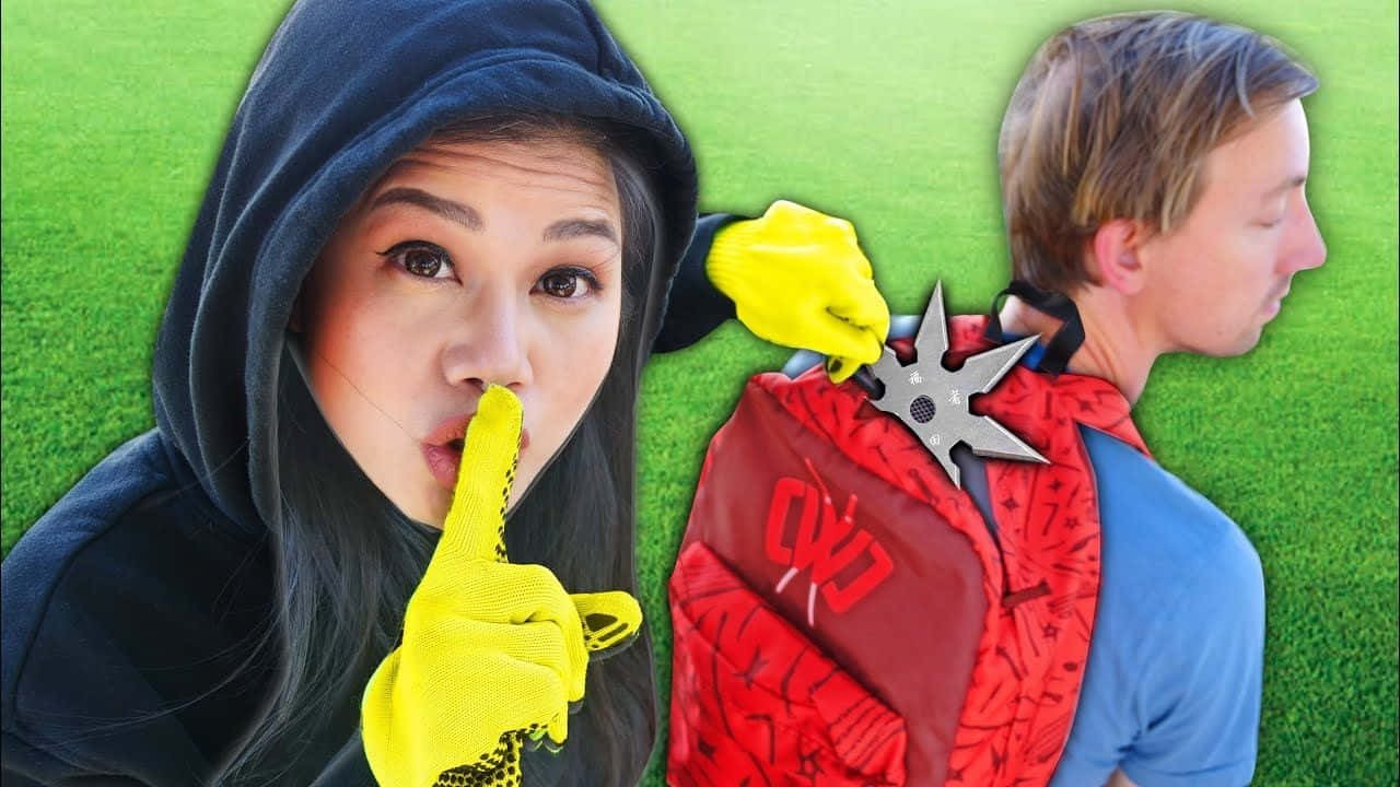 身穿黑色連帽衫和黃色手套的女子將手裏劍抵在男子背後，同時做出噤聲手勢。