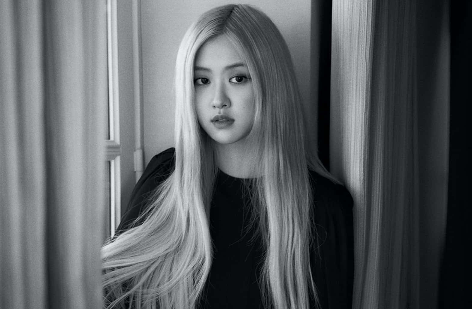 長金髮女性站在窗簾之間的黑白肖像。