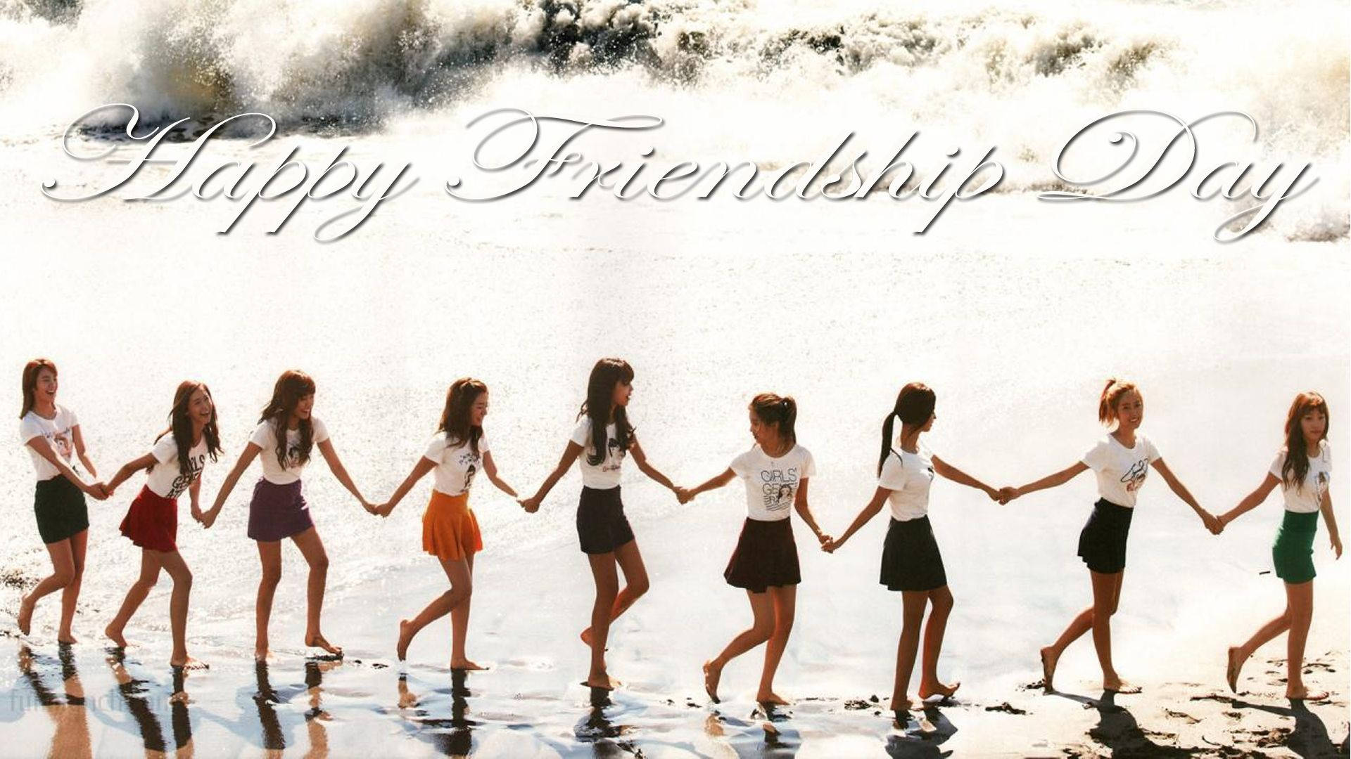 九個女孩在陽光明媚的海灘上手牽手，身後有海浪。