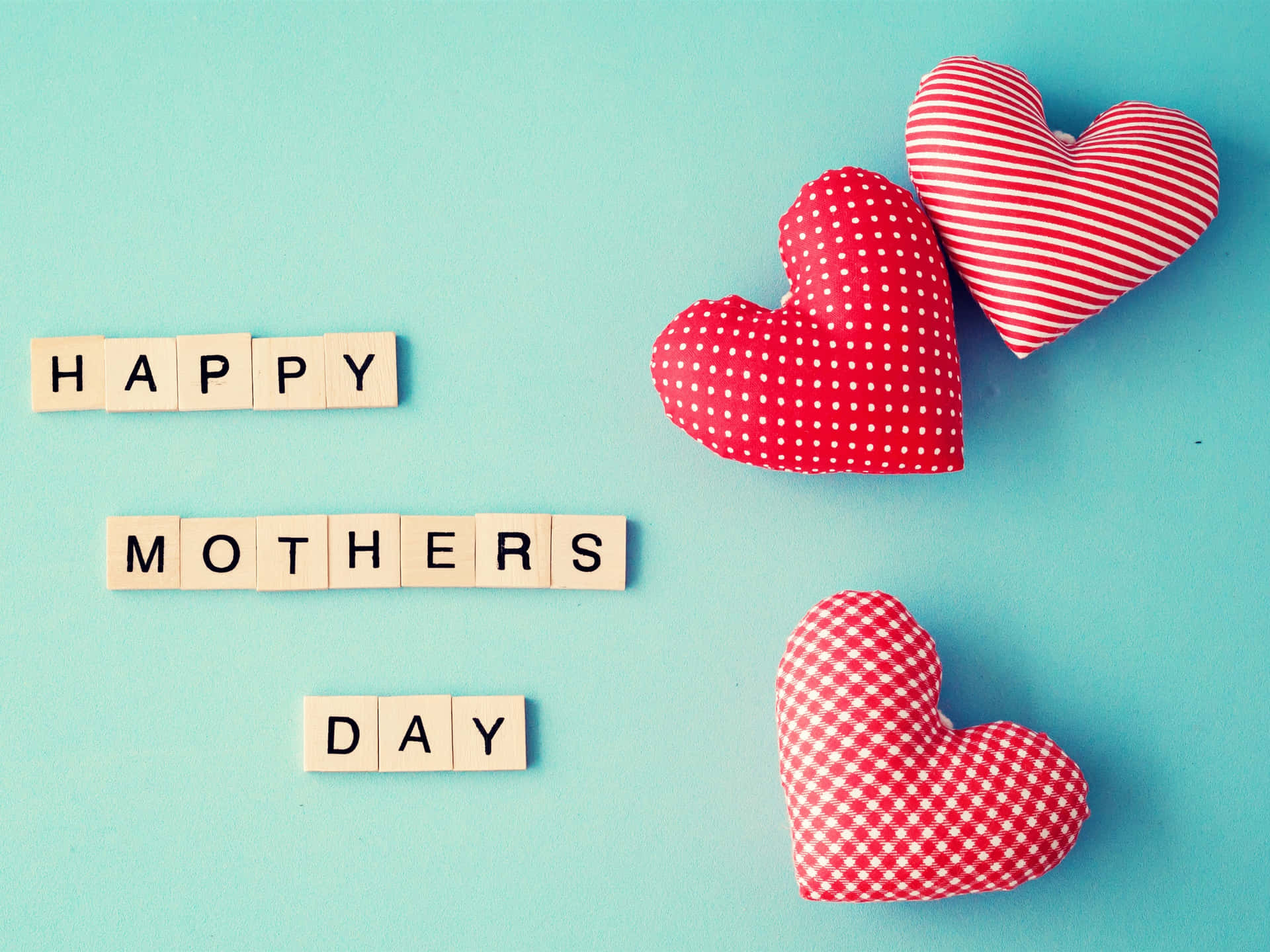 用木製拼字磚和三個紅色圖案心形在藍色上拼出的 Happy Mothers Day。