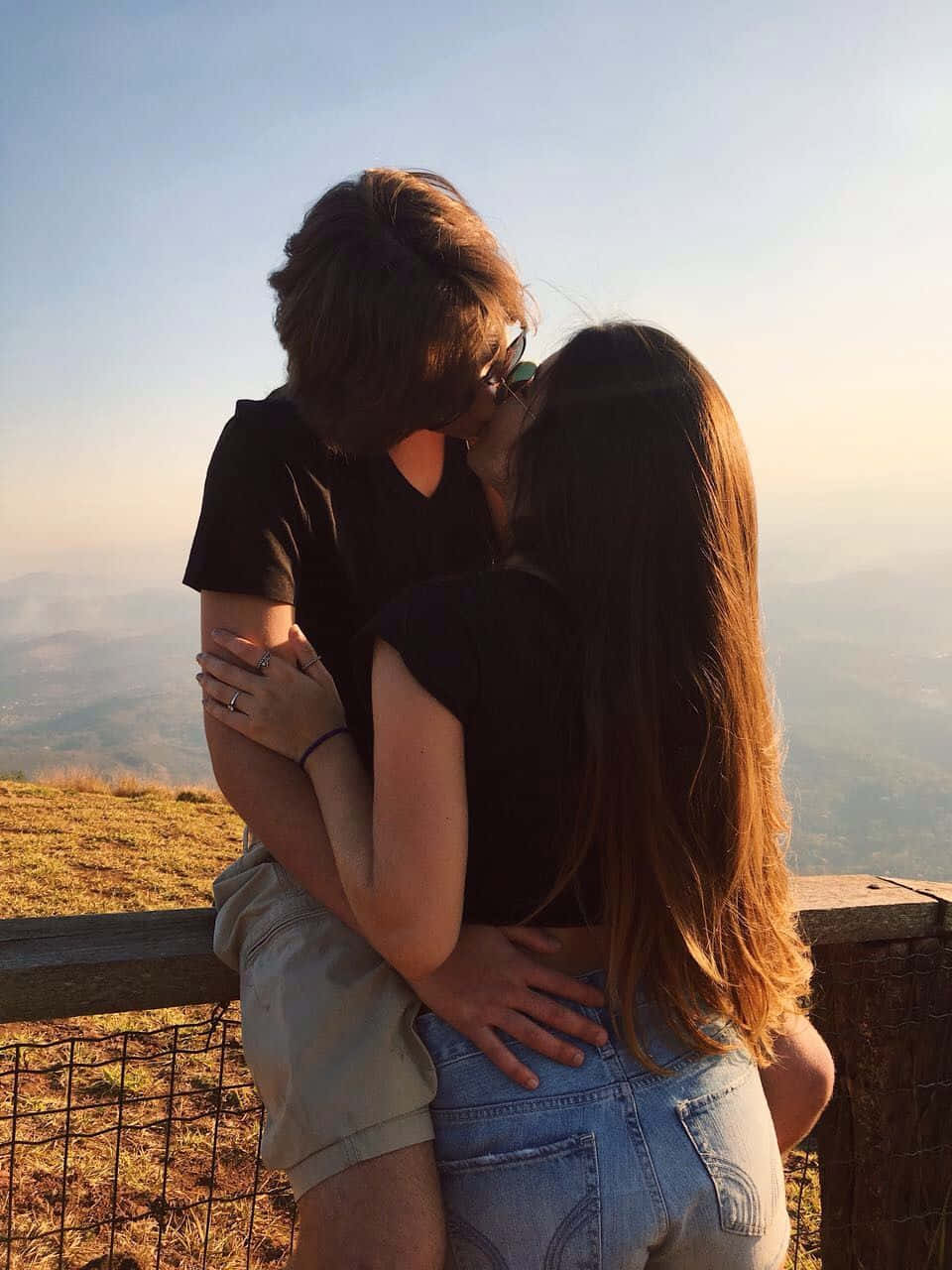 慶祝愛情 壁紙 — 一對情侶在山頂上擁抱親吻，俯瞰夕陽下煙霧瀰漫的山谷。