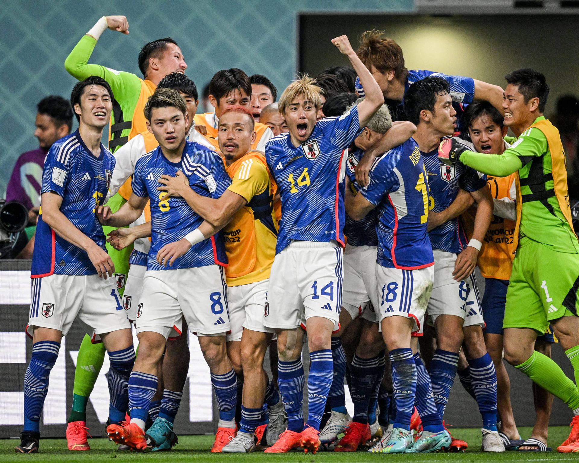 慶祝日本國家足球隊勝利 壁紙 — 日本足球運動員身穿藍色球衣，在球場燈光下的綠色草地上一起狂歡慶祝。