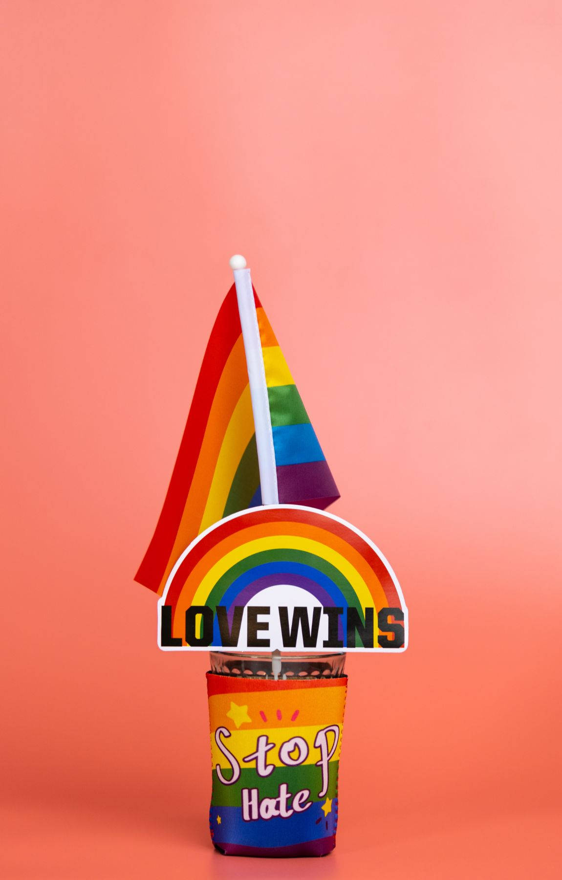 慶祝真實的自我 壁紙 — 彩虹旗和「LOVE WINS」標誌點綴著一個帶有「Stop Hate」文字的杯子，背景為柔和的粉紅色。