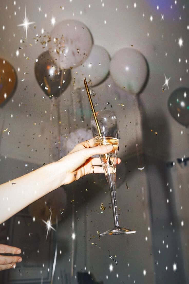 慶祝香檳祝酒派對氛圍 壁紙 — 一隻手拿著香檳杯，金色紙屑和星光燈光在飄浮的氣球周圍灑落。