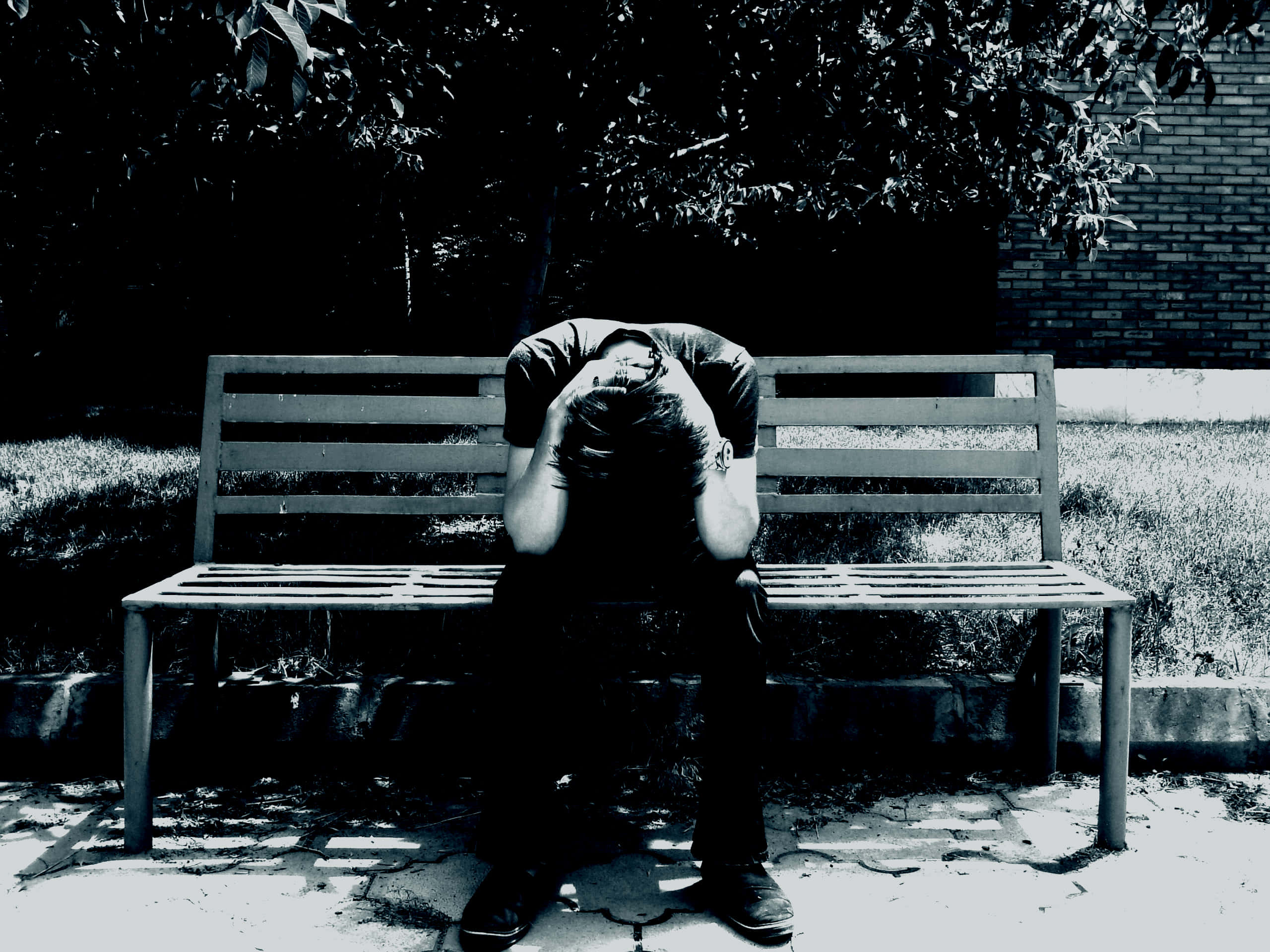 憂鬱少年獨坐長凳哭泣 壁紙 — 一個人蜷縮在公園長椅上，頭埋在手臂中，呈現鮮明的黑白對比。