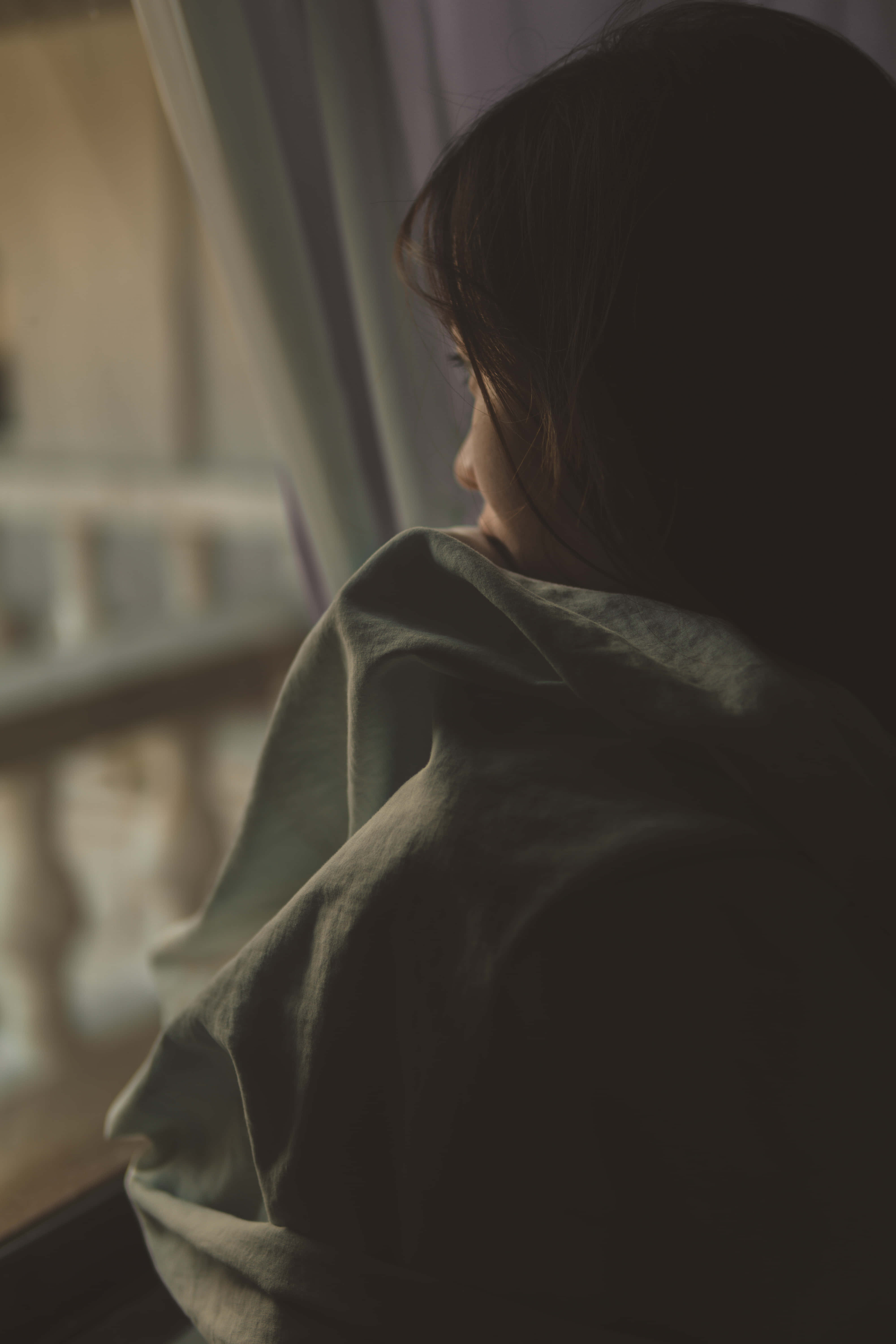「憂鬱極度孤立，讓人覺得自己無處容身」 壁紙 — 一個人裹著柔軟的毯子，若有所思地望著窗外，窗外沐浴在溫暖的金色光芒中。