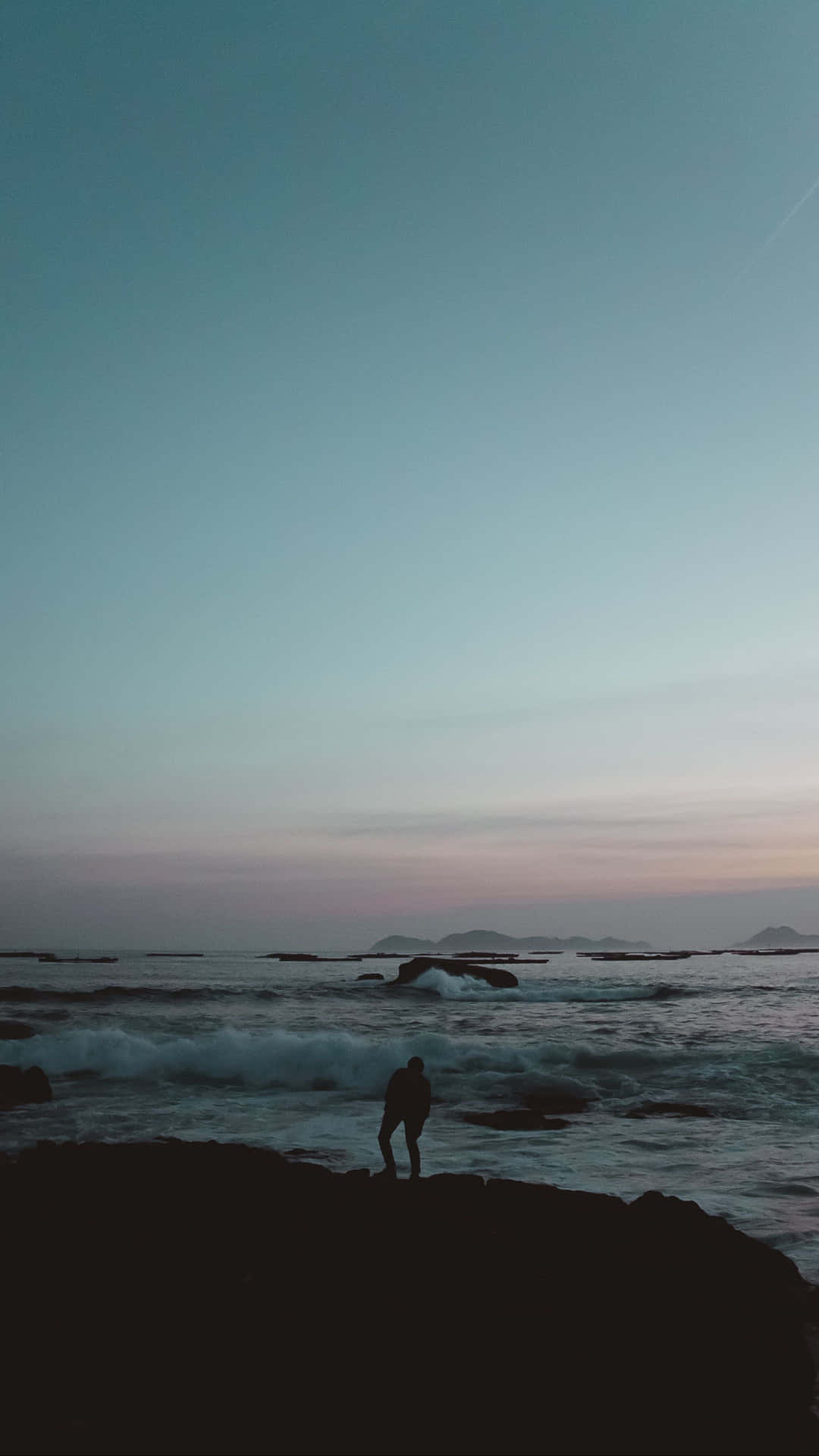 人站在岩石上觀看黃昏的海浪