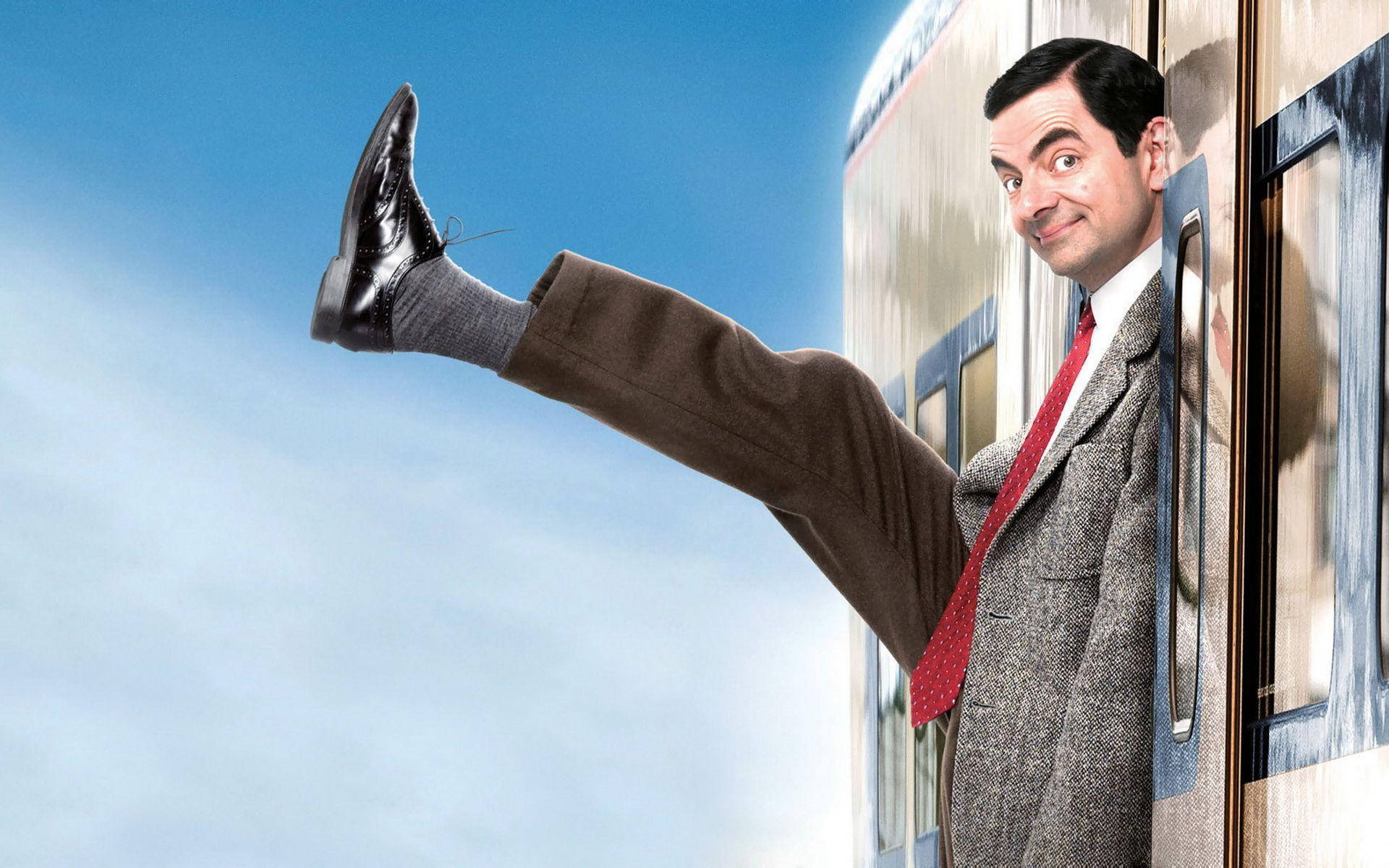 憨豆先生假期下火車 壁紙 — Mr. Bean 頑皮地將腿伸出火車窗外，背景是明亮的藍天。