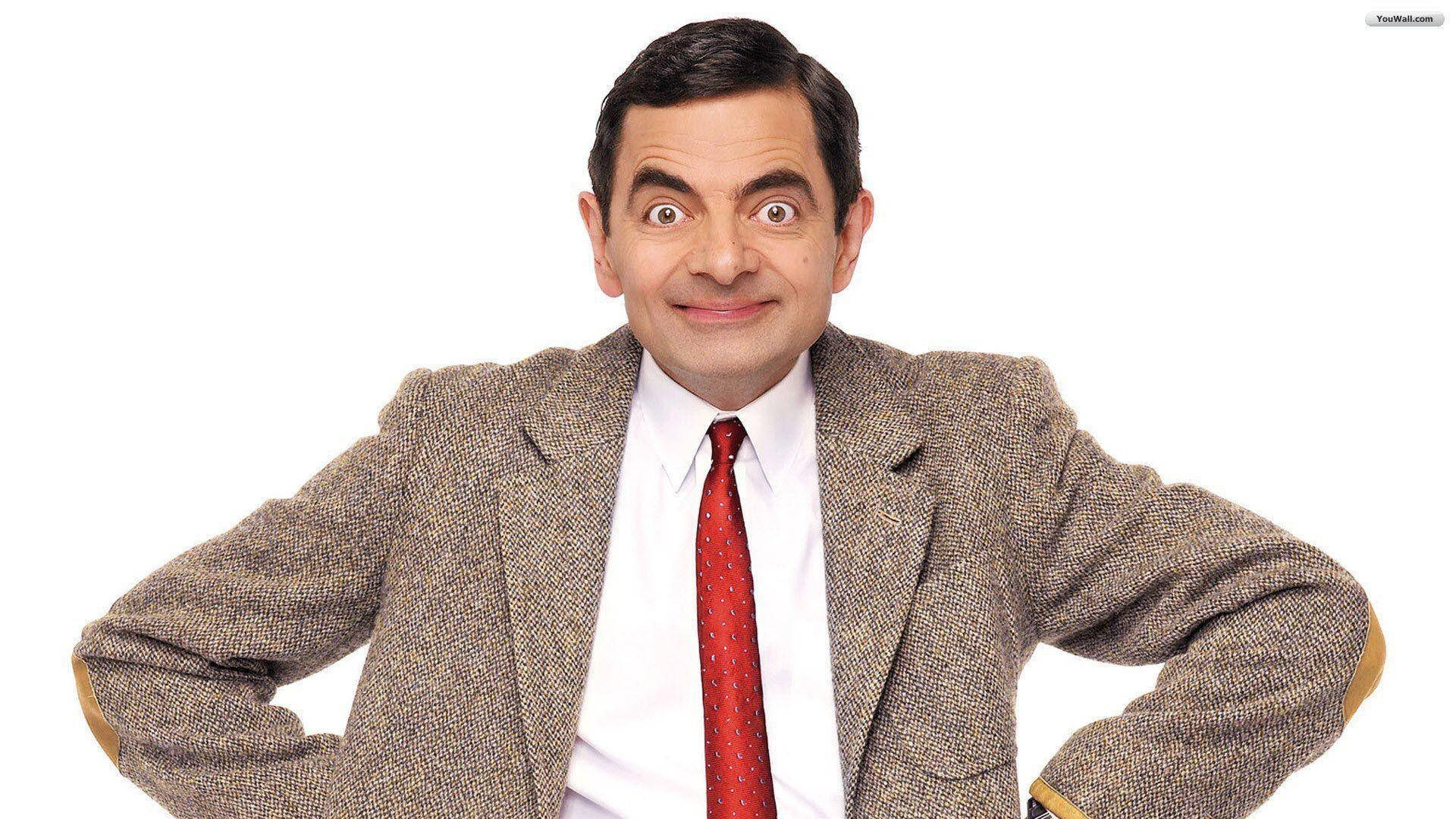憨豆先生搖擺姿勢 壁紙 — Mr Bean 穿著粗花呢外套和紅色領帶，在純白色背景前睜大眼睛、露出狡黠笑容，擺出滑稽姿勢。