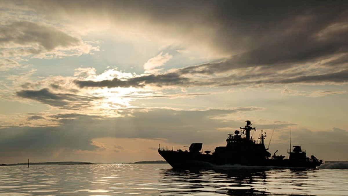 金色日落和戲劇性雲層中，軍艦在水上航行的剪影。
