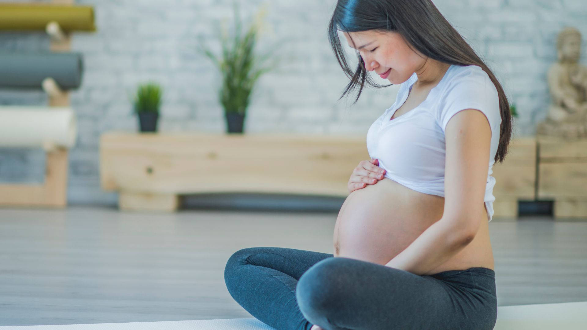 孕婦盤腿坐在瑜伽墊上，在寧靜的工作室中抱著肚子。