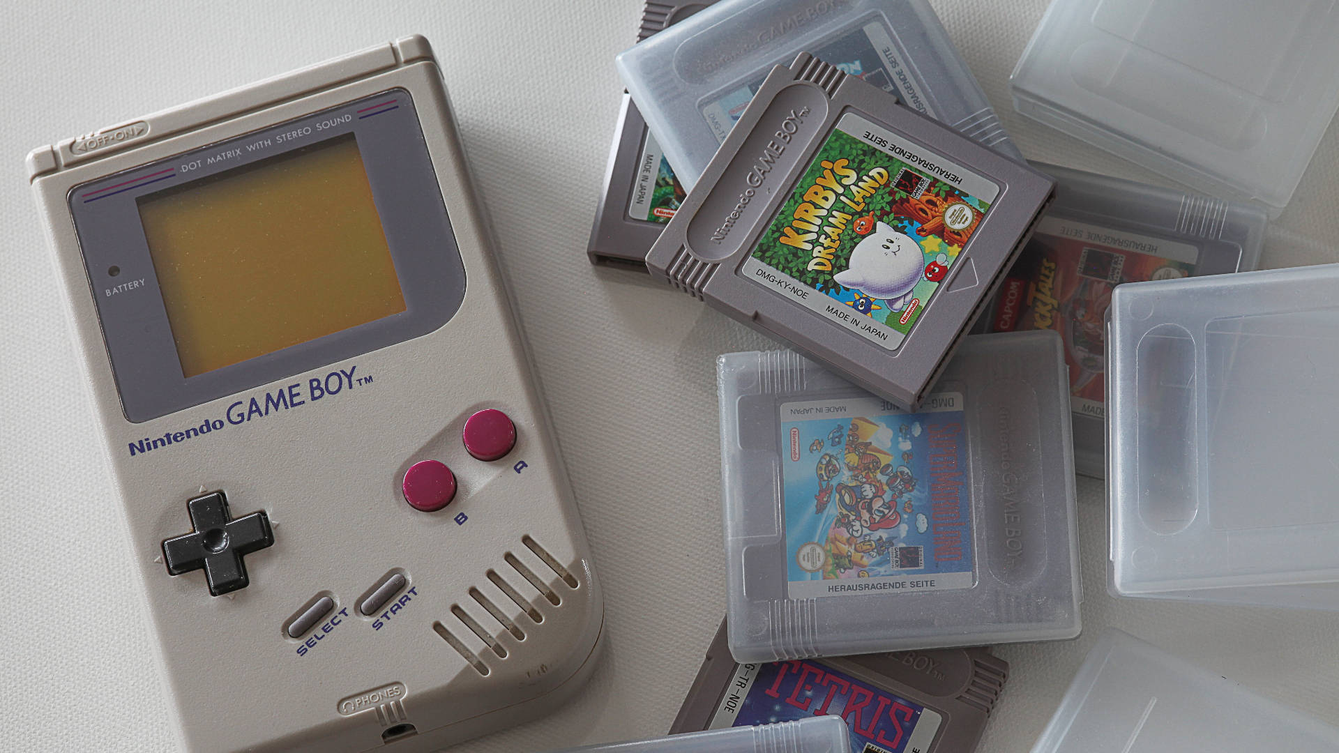 懷舊Game Boy與遊戲卡帶收藏 壁紙 — 米色 Game Boy 連同卡帶，包括 Kirby's Dream Land 和 Tetris，散落在白色表面上。