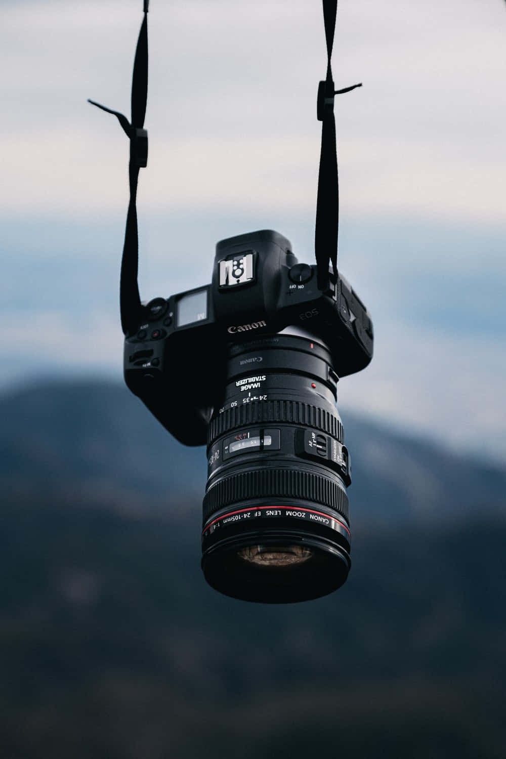 一部黑色 DSLR 相機用帶子懸掛在山景天空前。