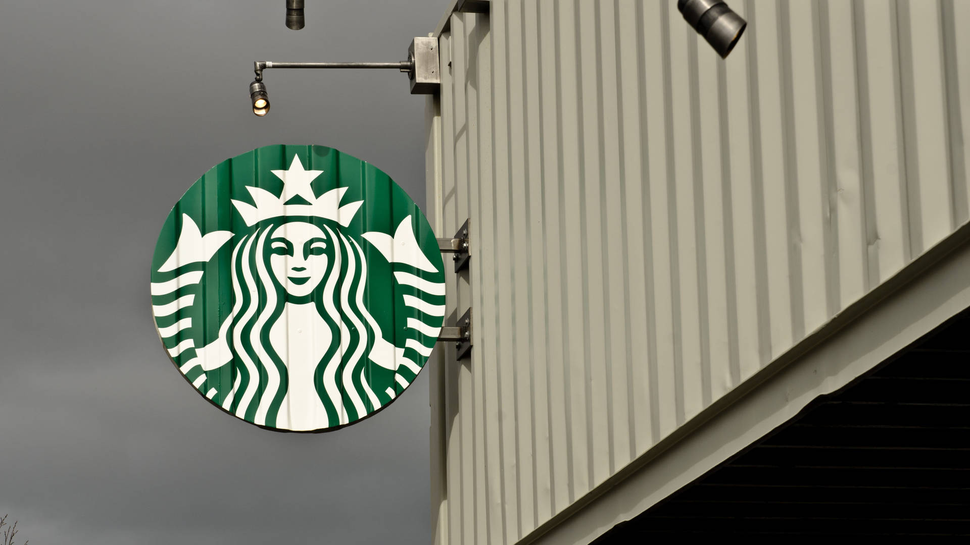 Starbucks標誌牌掛在金屬建築上，灰色天空