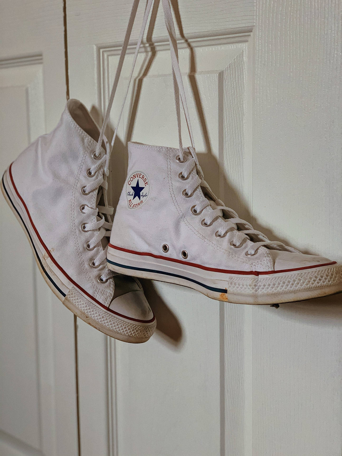 磨損的白色Converse運動鞋用鞋帶掛在白色門上。