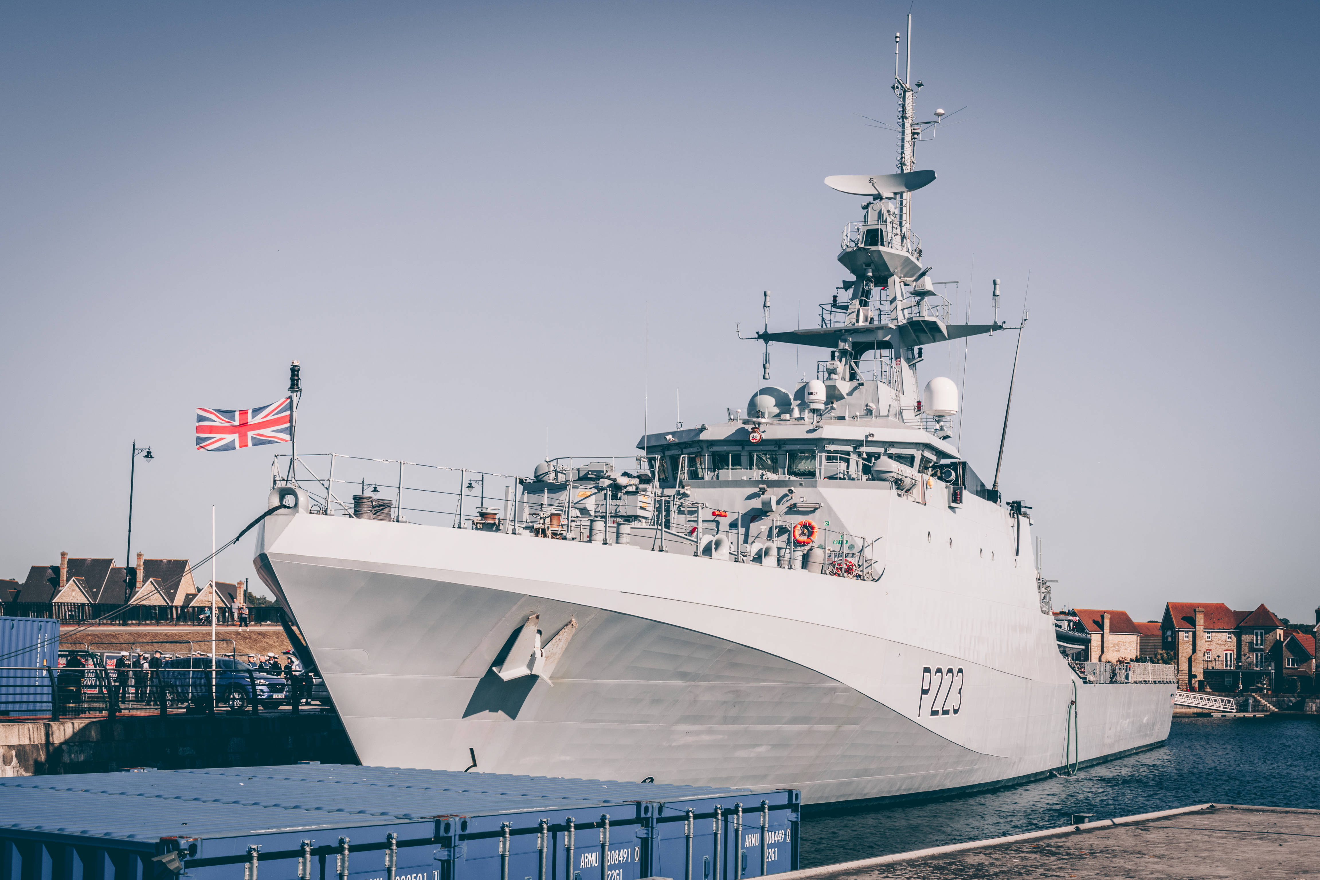 懸掛英國國旗的戰艦 壁紙 — 一艘時尚的灰色海軍軍艦，懸掛英國國旗，在平靜的港灣中驕傲地航行，天空湛藍。