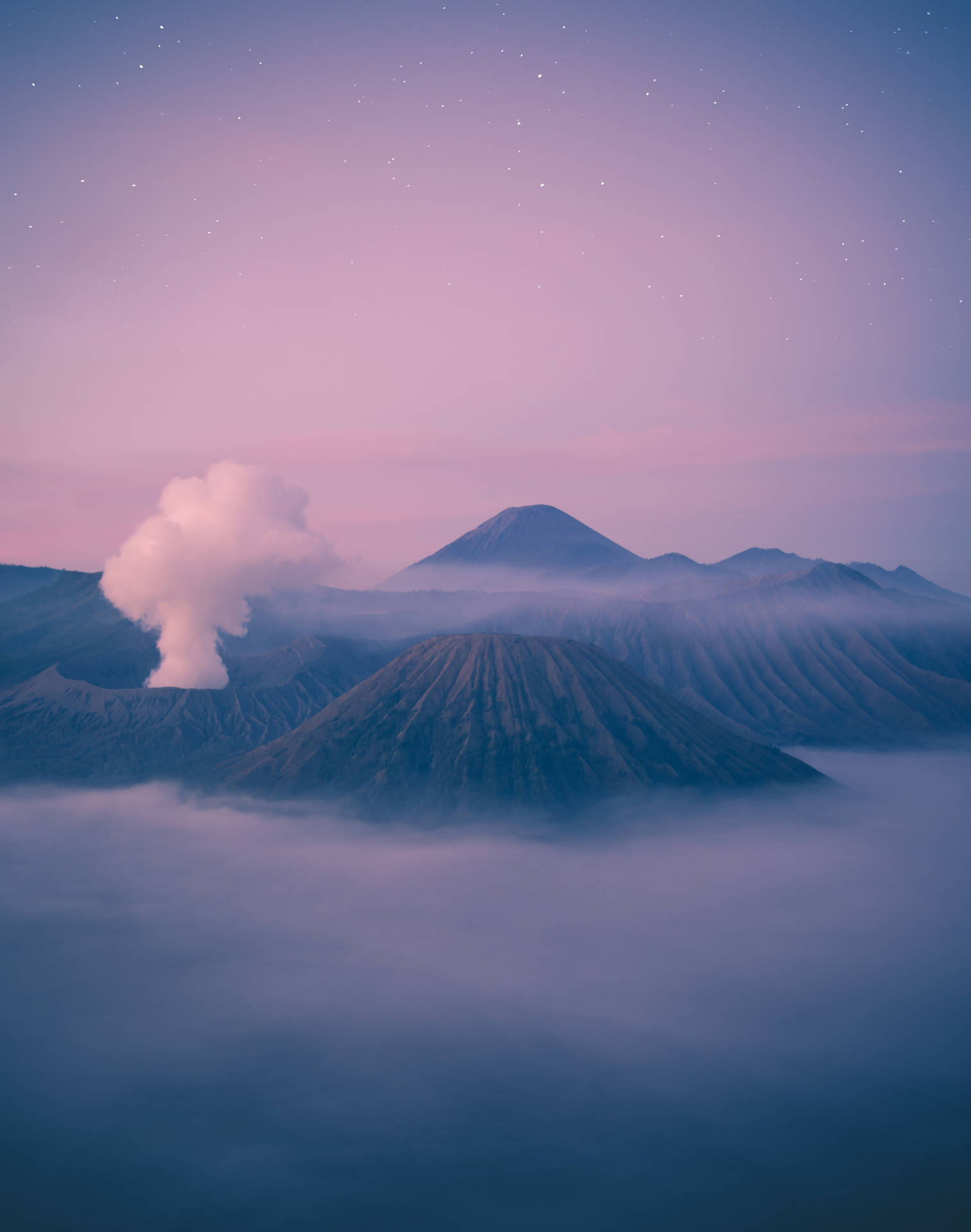 懸浮於山巔的夢幻馬卡龍雲朵 壁紙 — 火山從雲海中升起，在繁星點點的粉紫暮色天空下