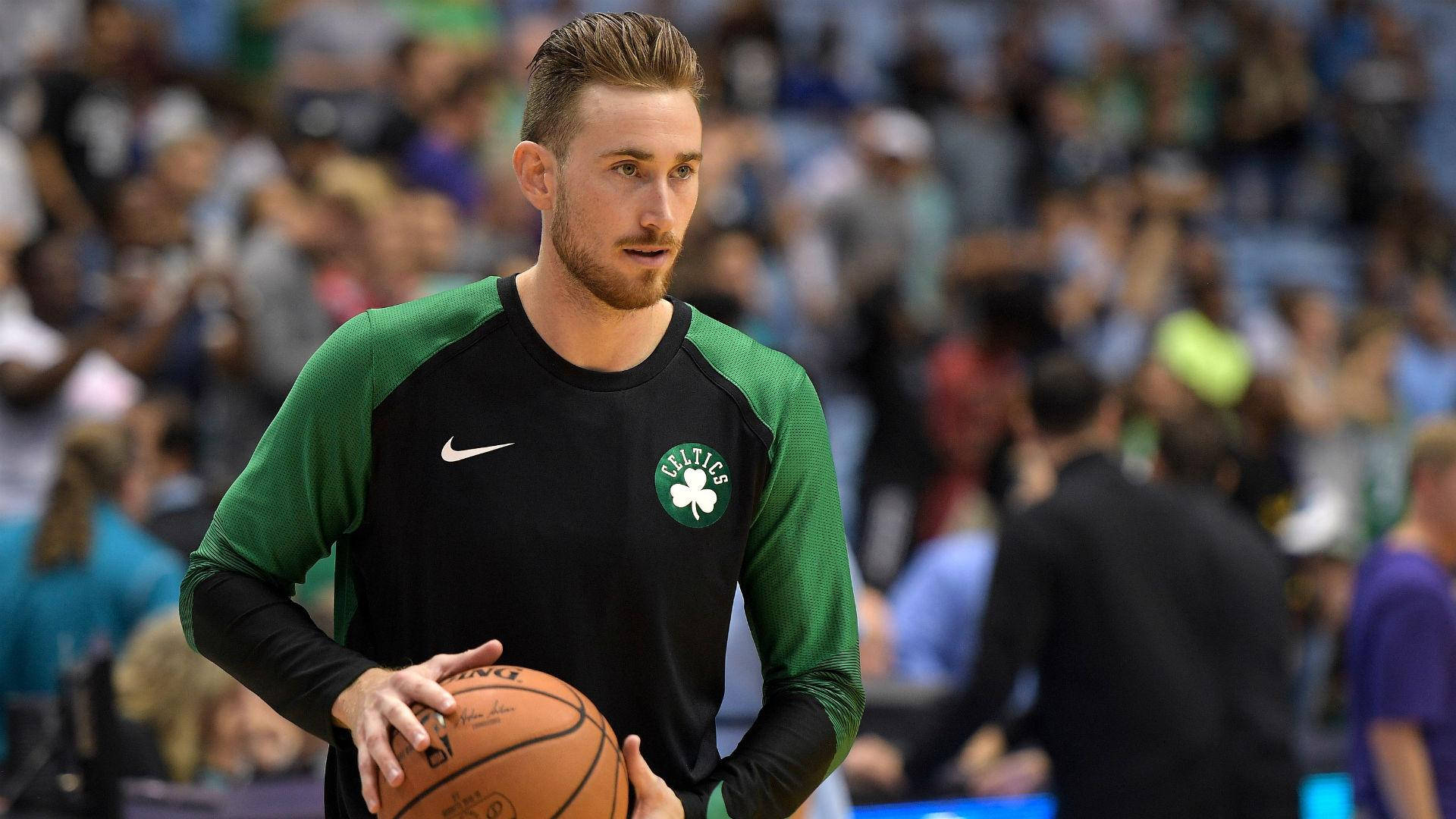 戈登·海沃德 2019 NBA季前賽 壁紙 — 一名專注的籃球運動員穿著綠色和黑色的塞爾特人熱身衫，在球場上拿著球，背景有模糊的觀眾。